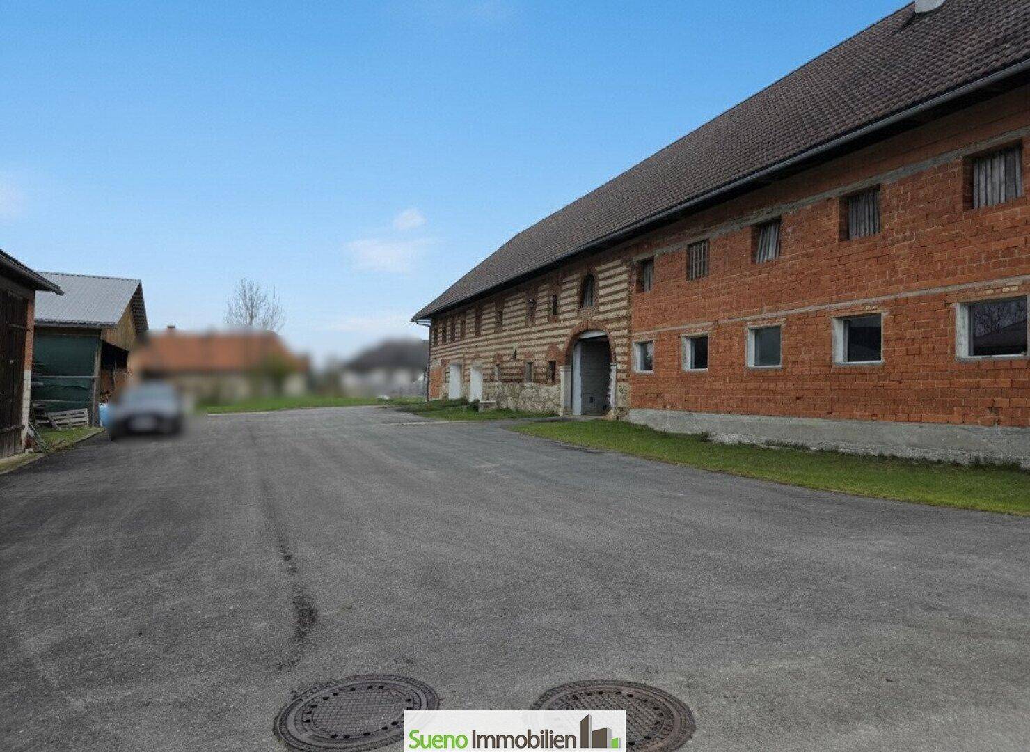 Lange Zufahrt zum Bauernhaus mit traditioneller Ziegelfassade und ländlicher Umgebung.