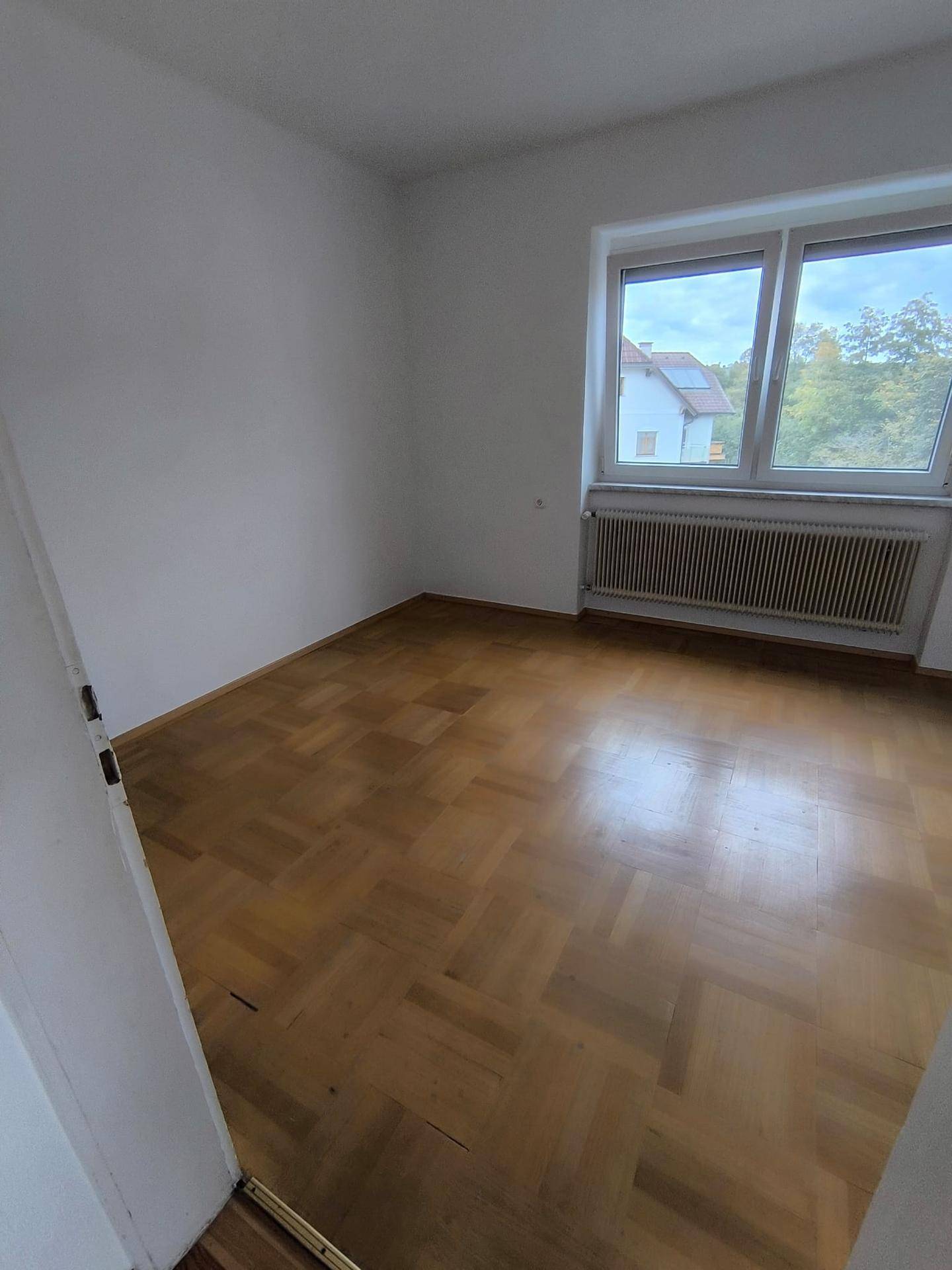 Ruhiges Zimmer mit Parkettboden und Fenster, bietet eine angenehme Atmosphäre für Erholung.
