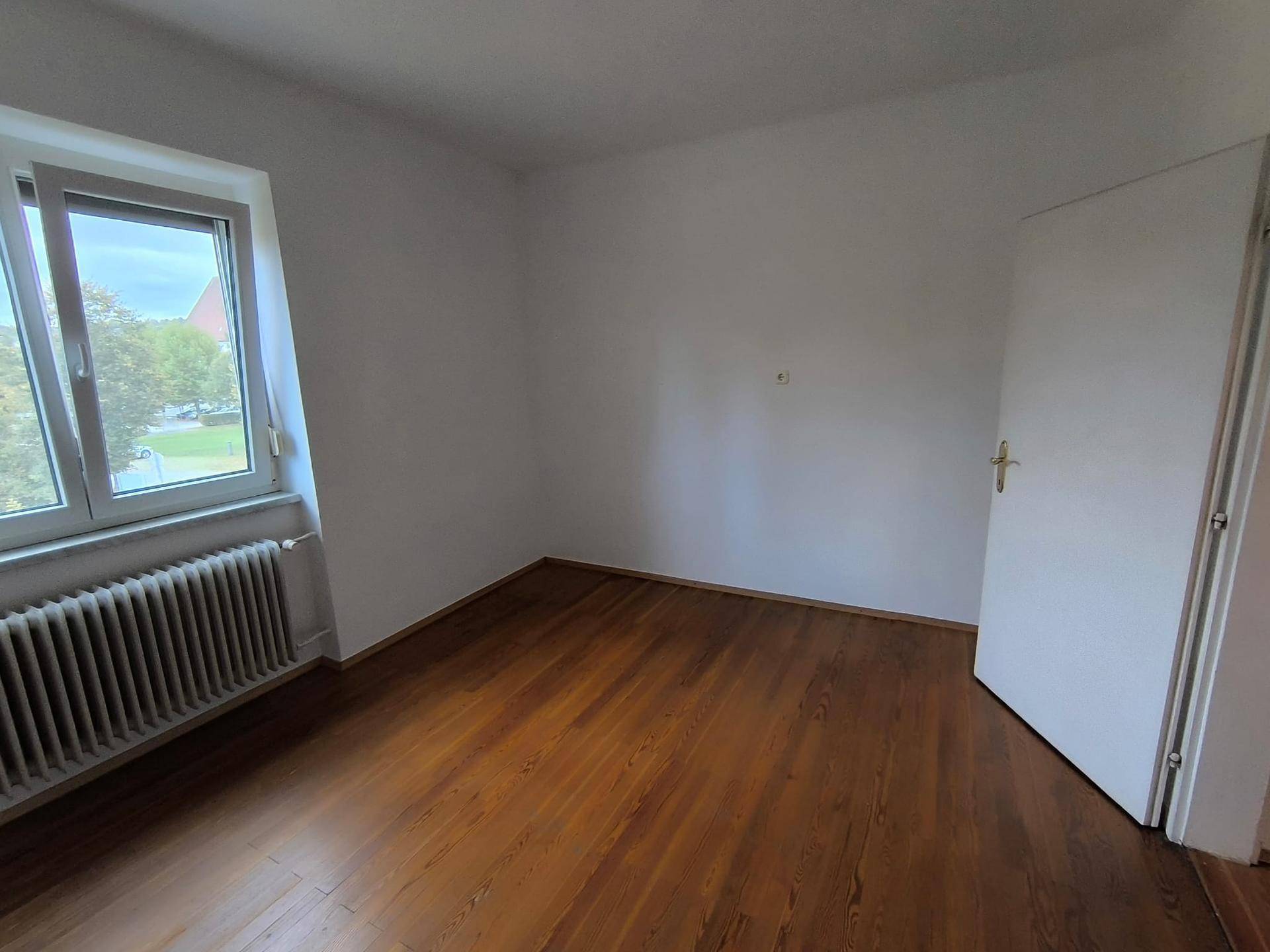 Zimmer mit dunklem Holzplankenboden und Fenster, bietet eine gemütliche und ruhige Atmosphäre.