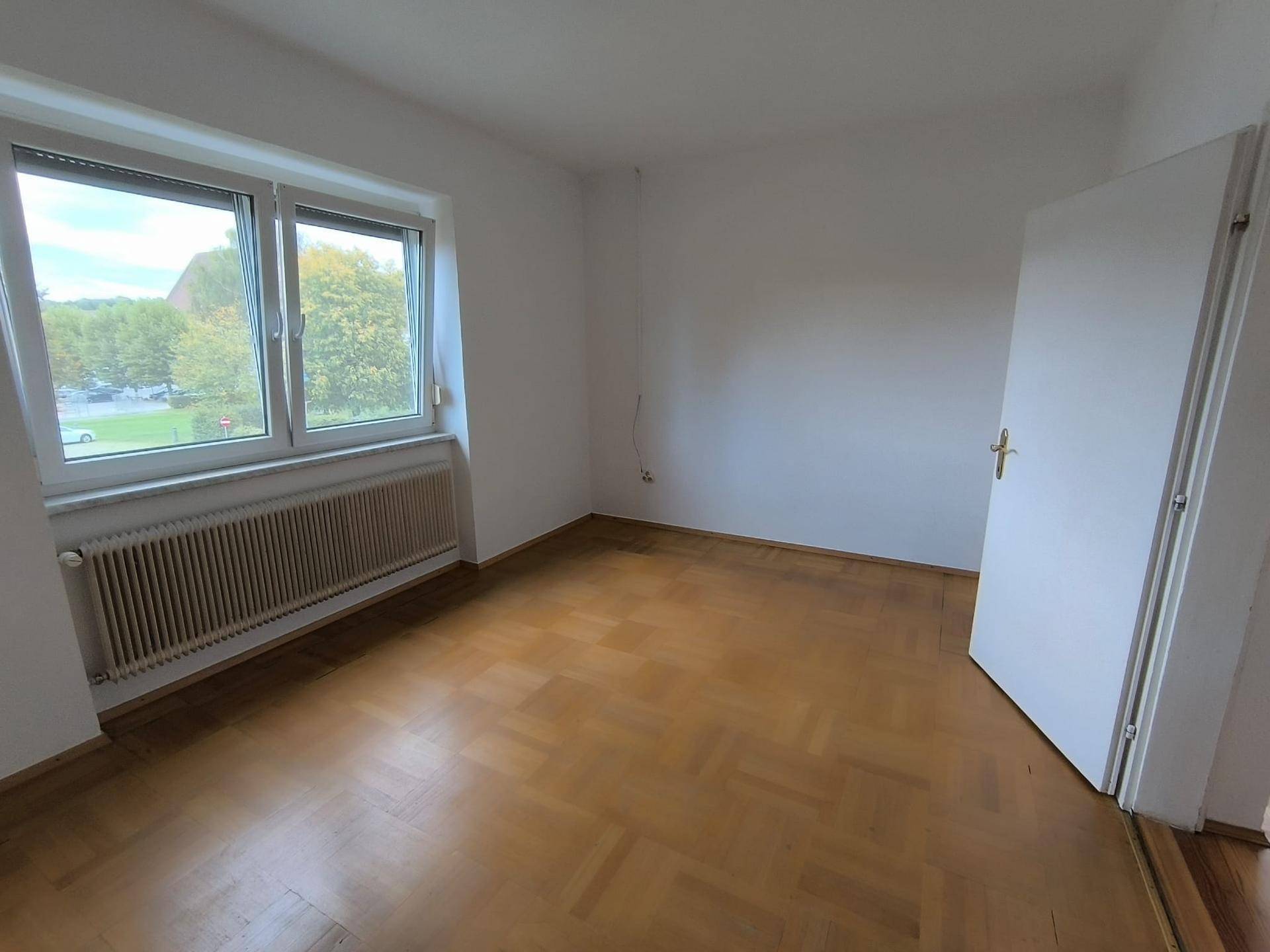 Geräumiges Zimmer mit Parkettboden und Fenster mit Blick ins Grüne, ideal als Schlafzimmer.