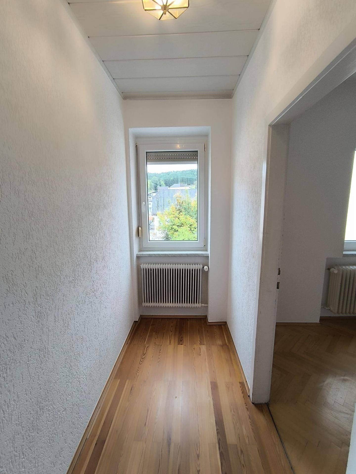 Heller Flur mit Holzplankenboden und einem Fenster am Ende, das Tageslicht hereinlässt.