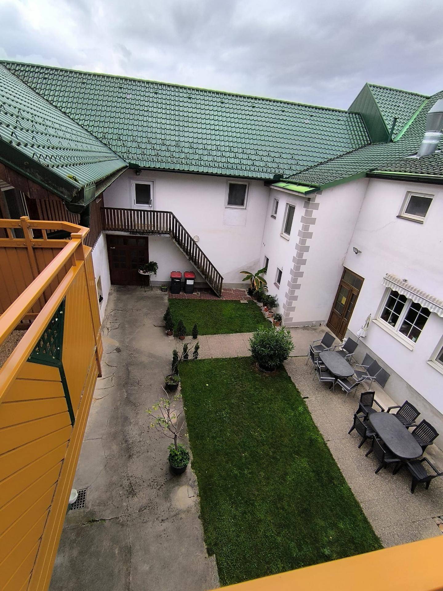 Innenhof mit Rasenflächen, gepflasterten Wegen und Sitzgelegenheiten, umgeben von Gebäuden mit grünem Dach.