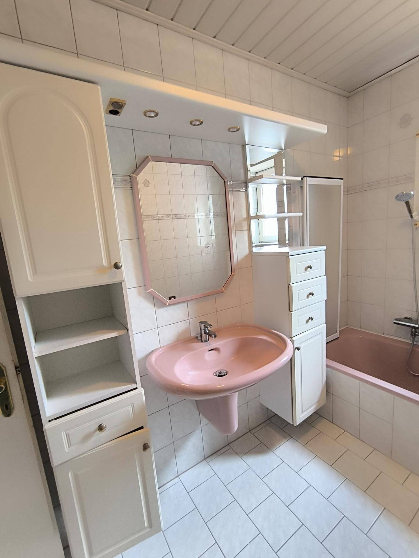 Badezimmer im 80er-Jahre-Stil mit rosa Waschbecken und Badewanne, weißen Fliesen und Holzdecke.