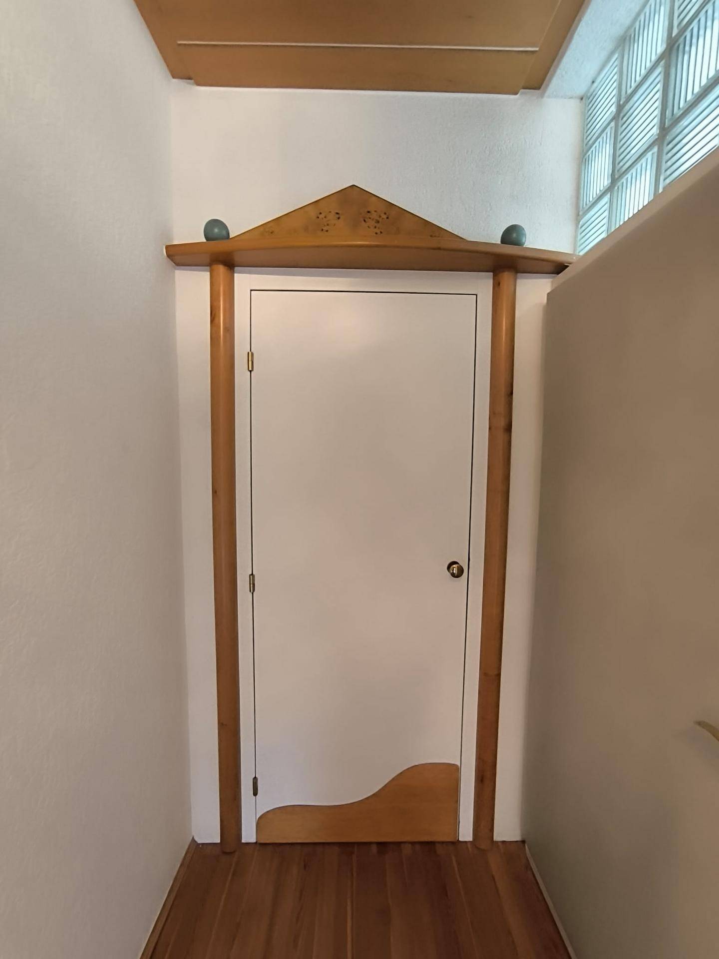 Dekorative Holztür führt zu einem kleinen Abstellraum, mit Glasbausteinen für zusätzliches Licht.