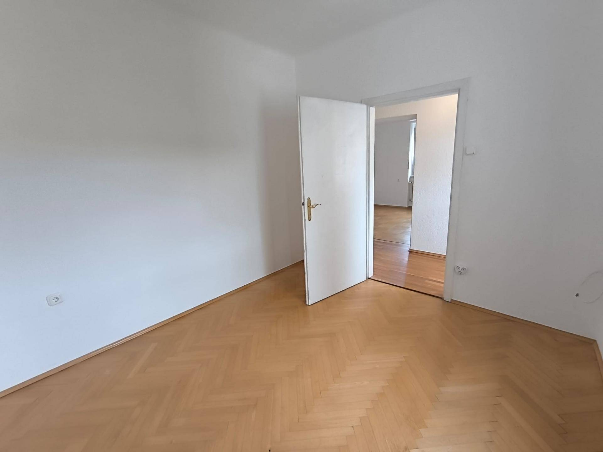 Leeres Zimmer mit Parkettboden und weiß gestrichenen Wänden, bietet vielseitige Nutzungsmöglichkeiten.