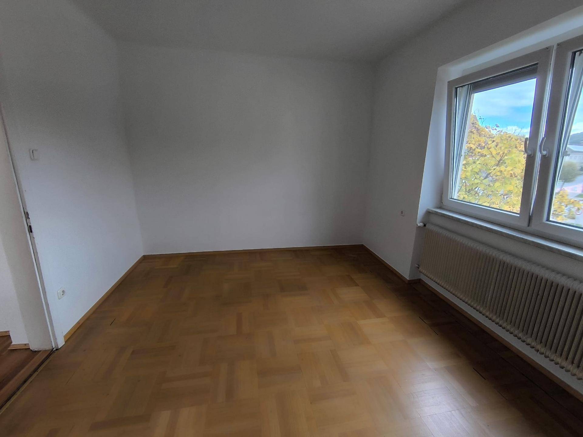 Helles Zimmer mit Parkettboden und großem Fenster, das viel natürliches Licht hereinlässt.