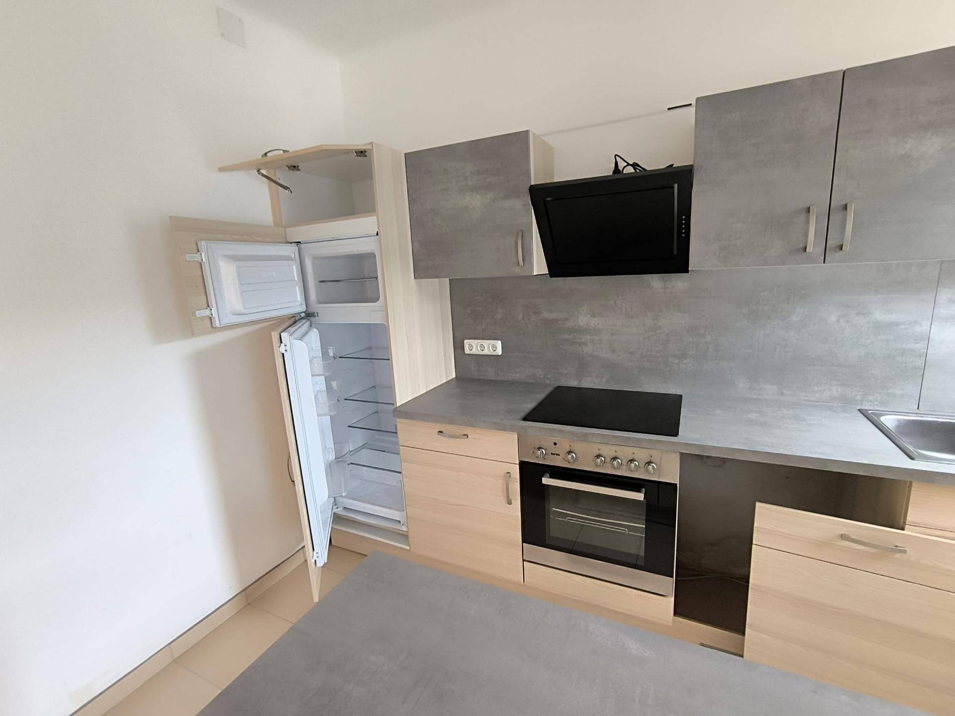 Helle Einbauküche mit modernen Holz- und Grautönen, ausgestattet mit Kühlschrank, Backofen und Kochfeld.