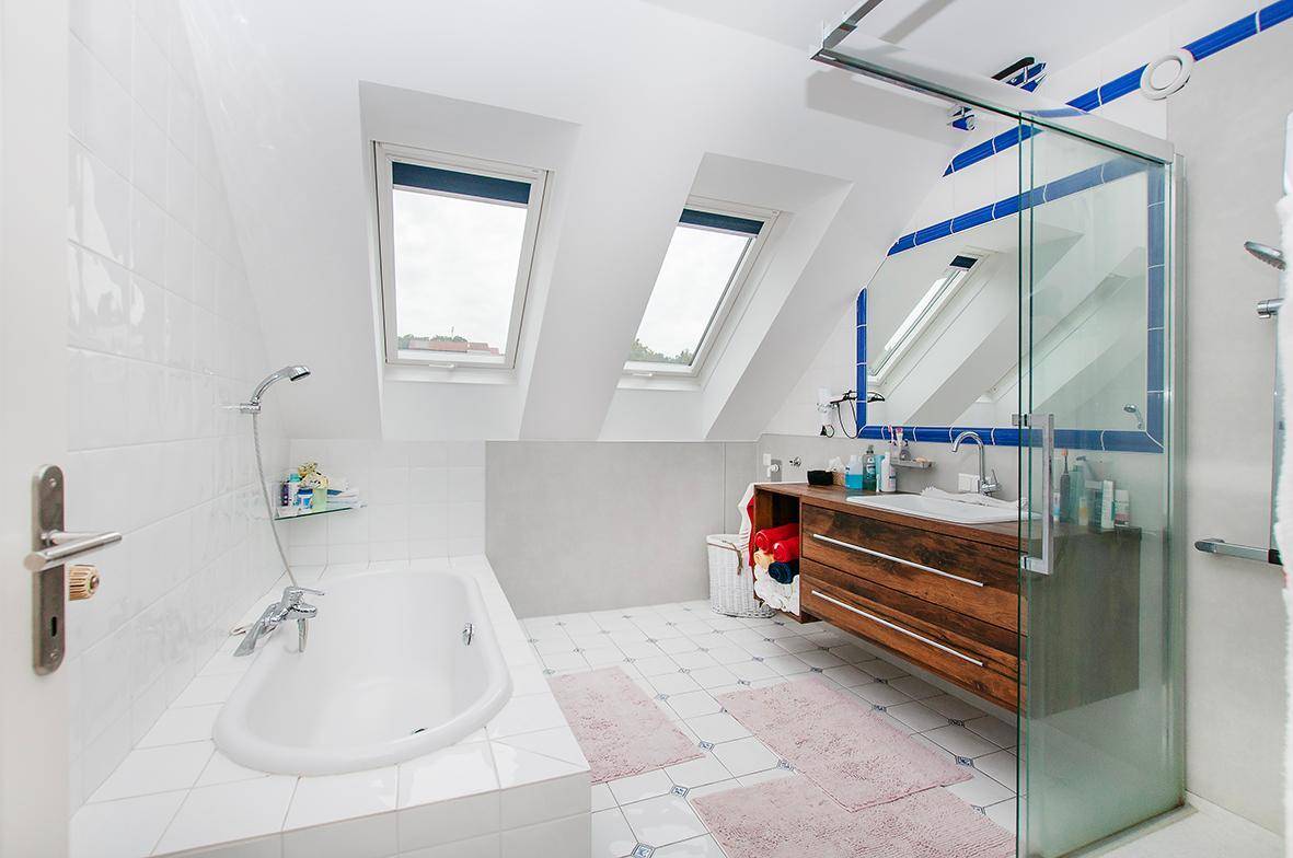 Helles Badezimmer mit Badewanne, Dusche, Holzwaschtisch und Dachfenstern.