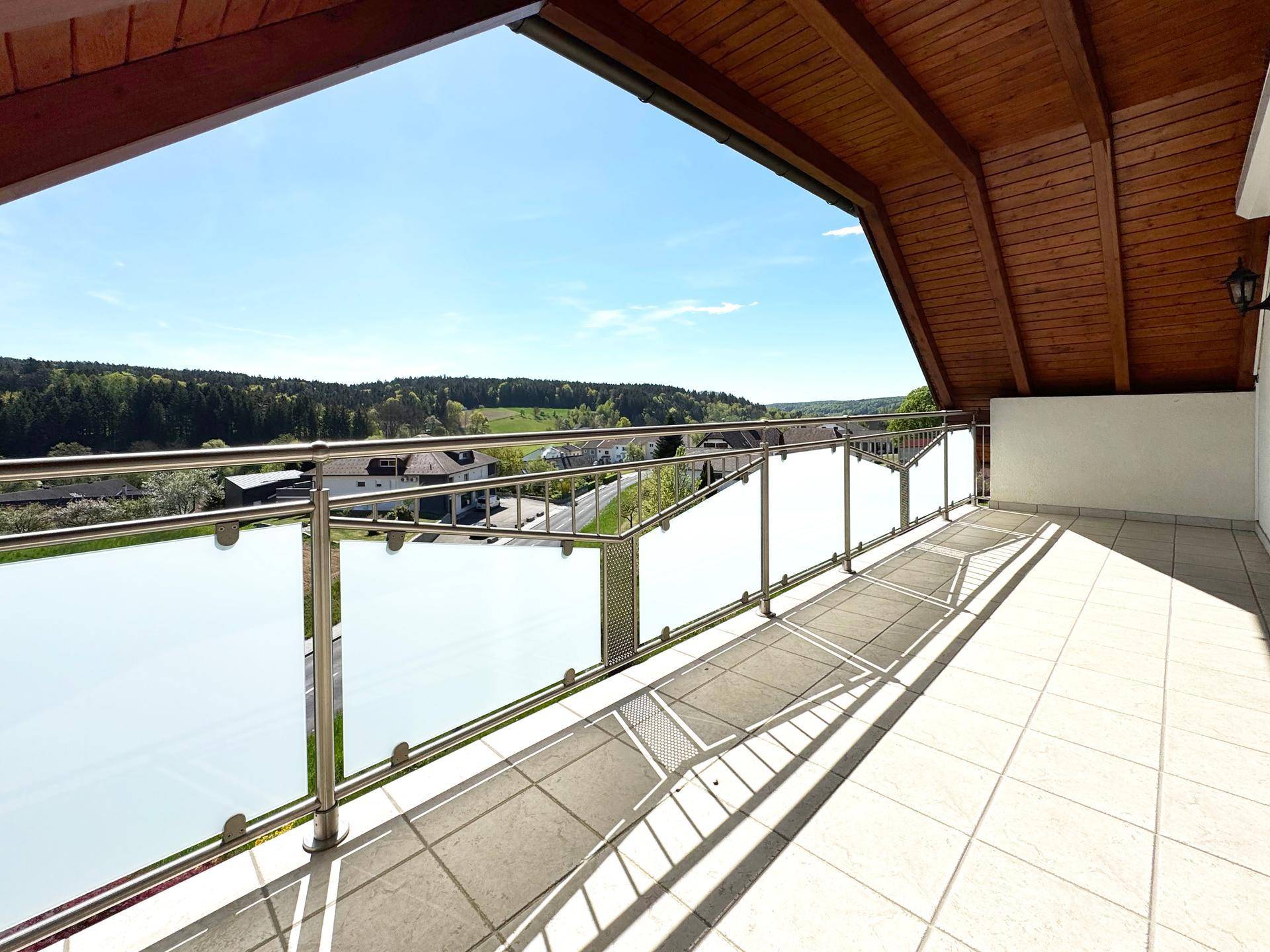 Geräumiger Balkon mit Fliesenboden, Holzdecke und weitem Blick über die Landschaft.