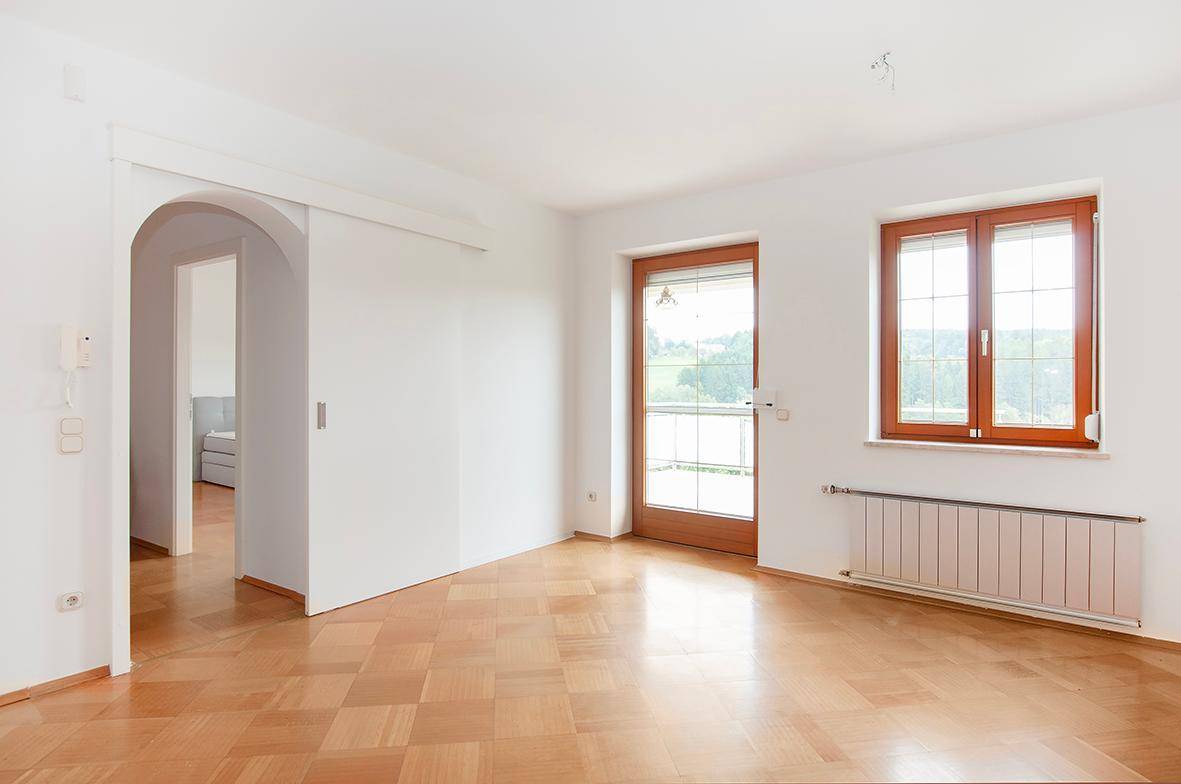 Heller Raum mit Parkettboden, Holztür und Fenster mit Blick ins Grüne.