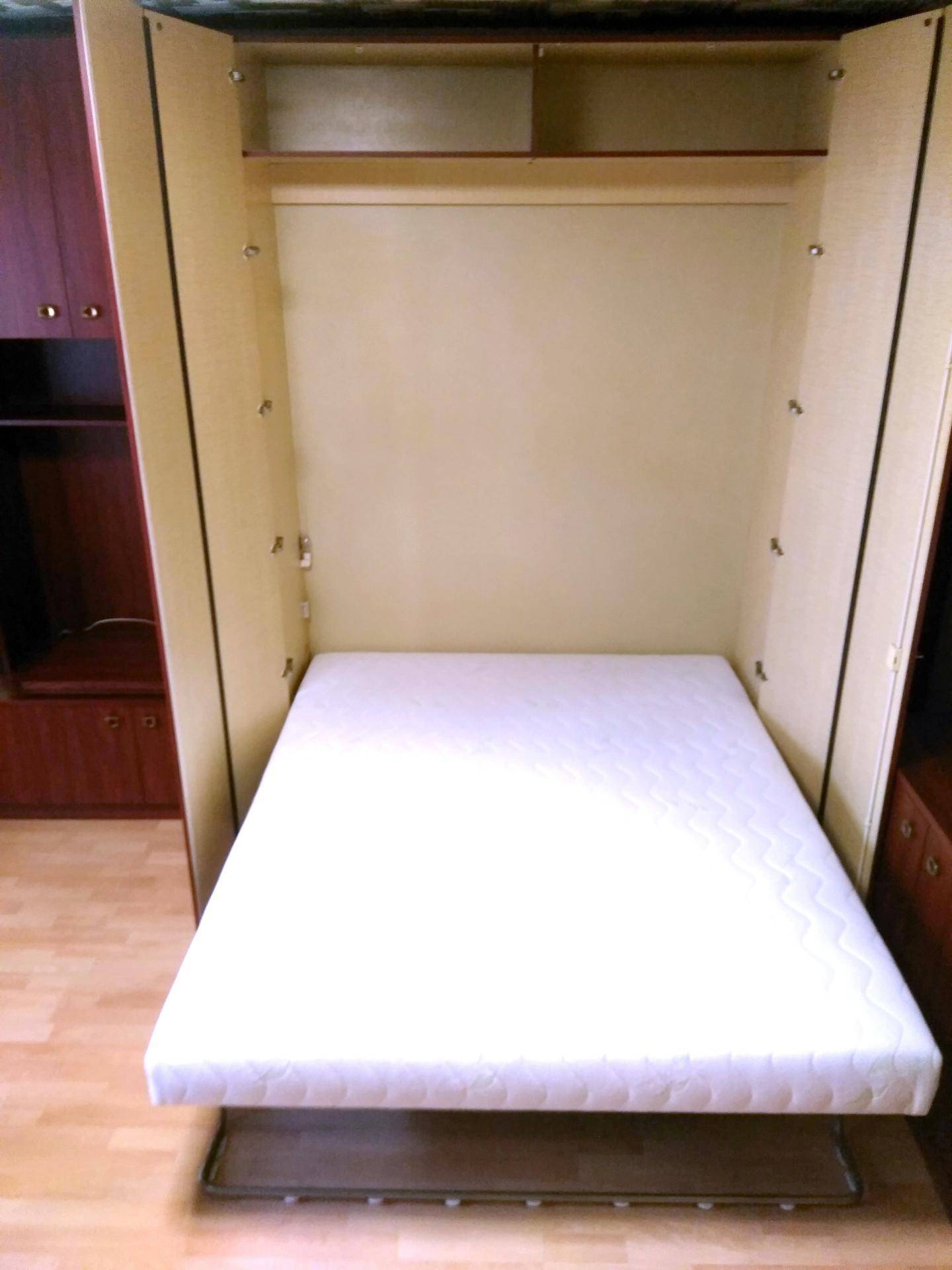 Klappbett in einem Schlafzimmer mit Holzschränken und Laminatboden.