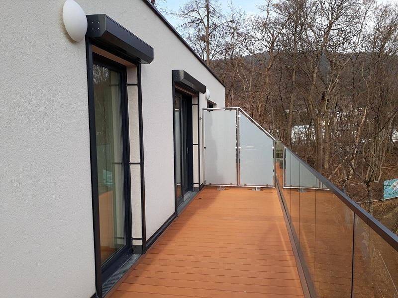 Außenansicht der modernen Fassade mit großen Fenstern, Rollläden und der weitläufigen Holzterrasse.