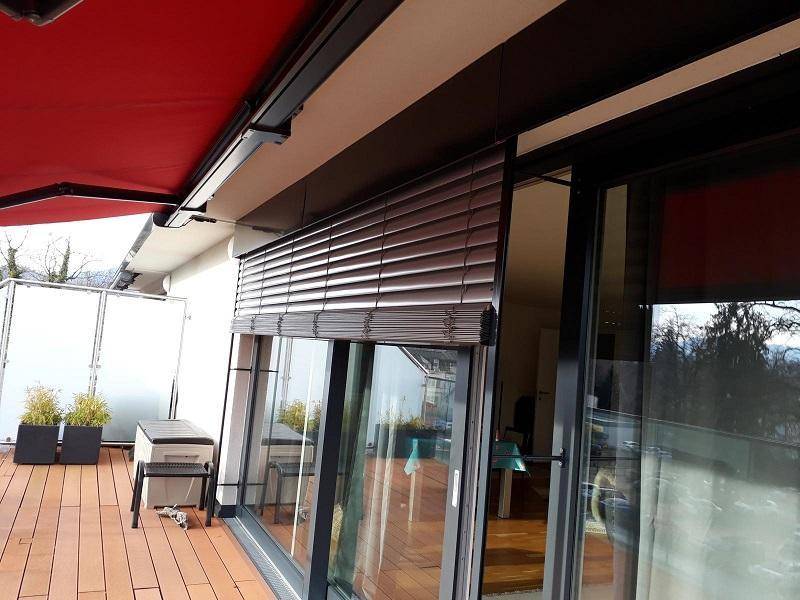 Detailansicht der Terrasse mit ausgefahrener Markise und heruntergelassenem Außenrollo an der großen Glasschiebetür.