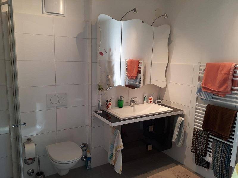 Modernes Badezimmer mit weißen Fliesen, wandhängendem WC, Waschtisch und beheiztem Handtuchhalter.