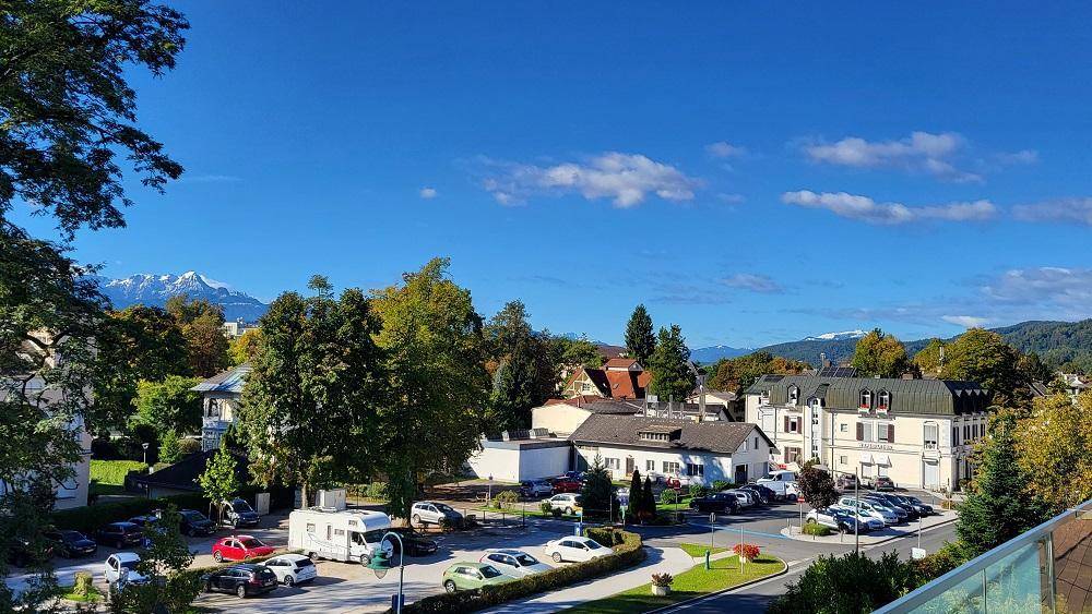 Panoramablick über eine grüne Stadtlandschaft mit Bergen im Hintergrund unter blauem Himmel.