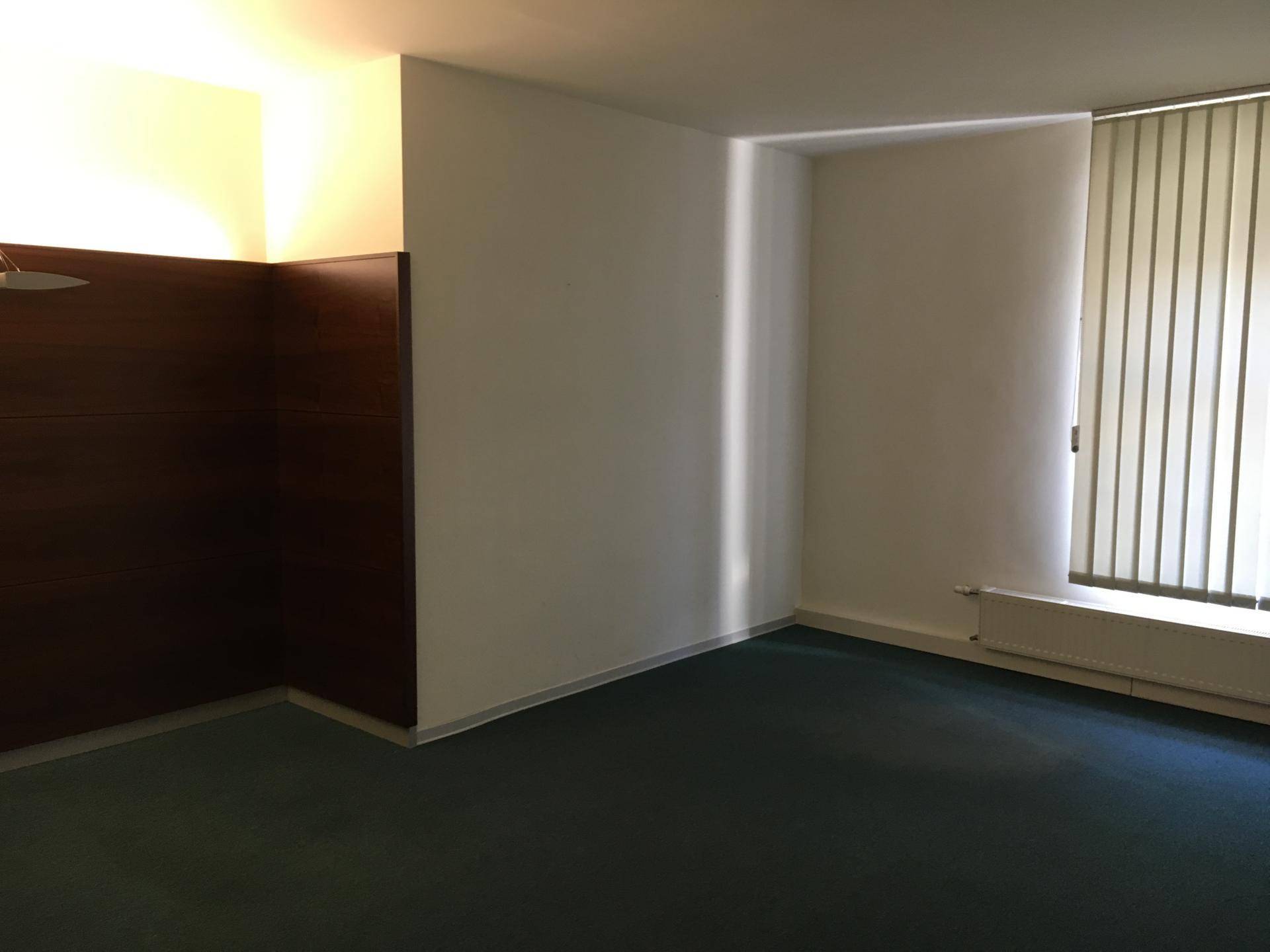 Büroraum mit dunkelgrünem Teppichboden, vertikalen Jalousien und einer dunklen Holzwandverkleidung.