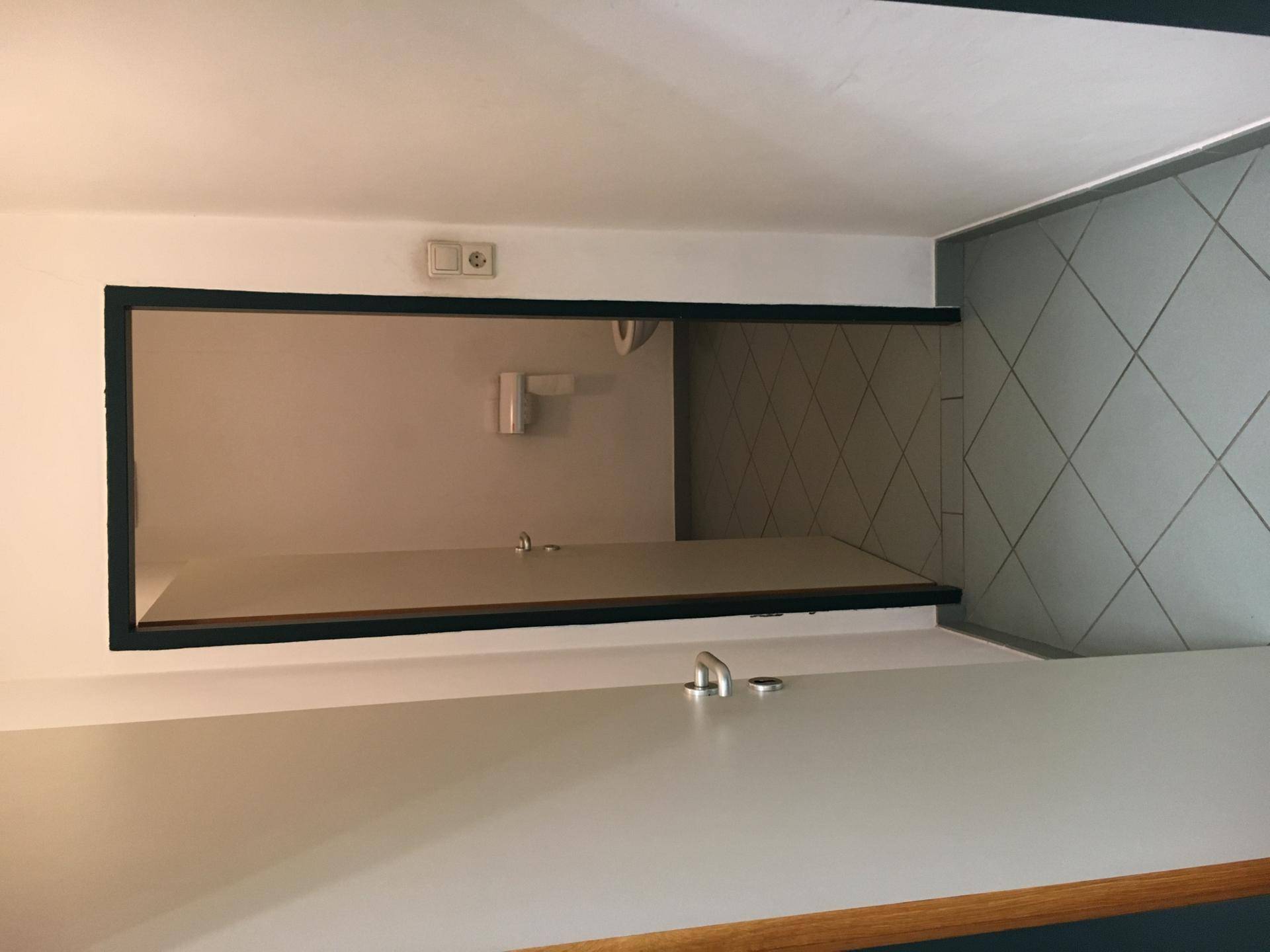Badezimmer mit hellgrauen Fliesen, einem Waschbecken und einer Toilette.
