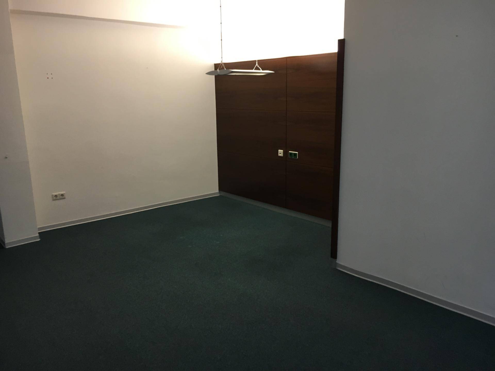 Leerer Büroraum mit dunkelgrünem Teppichboden und einer dunklen Holzwandverkleidung.