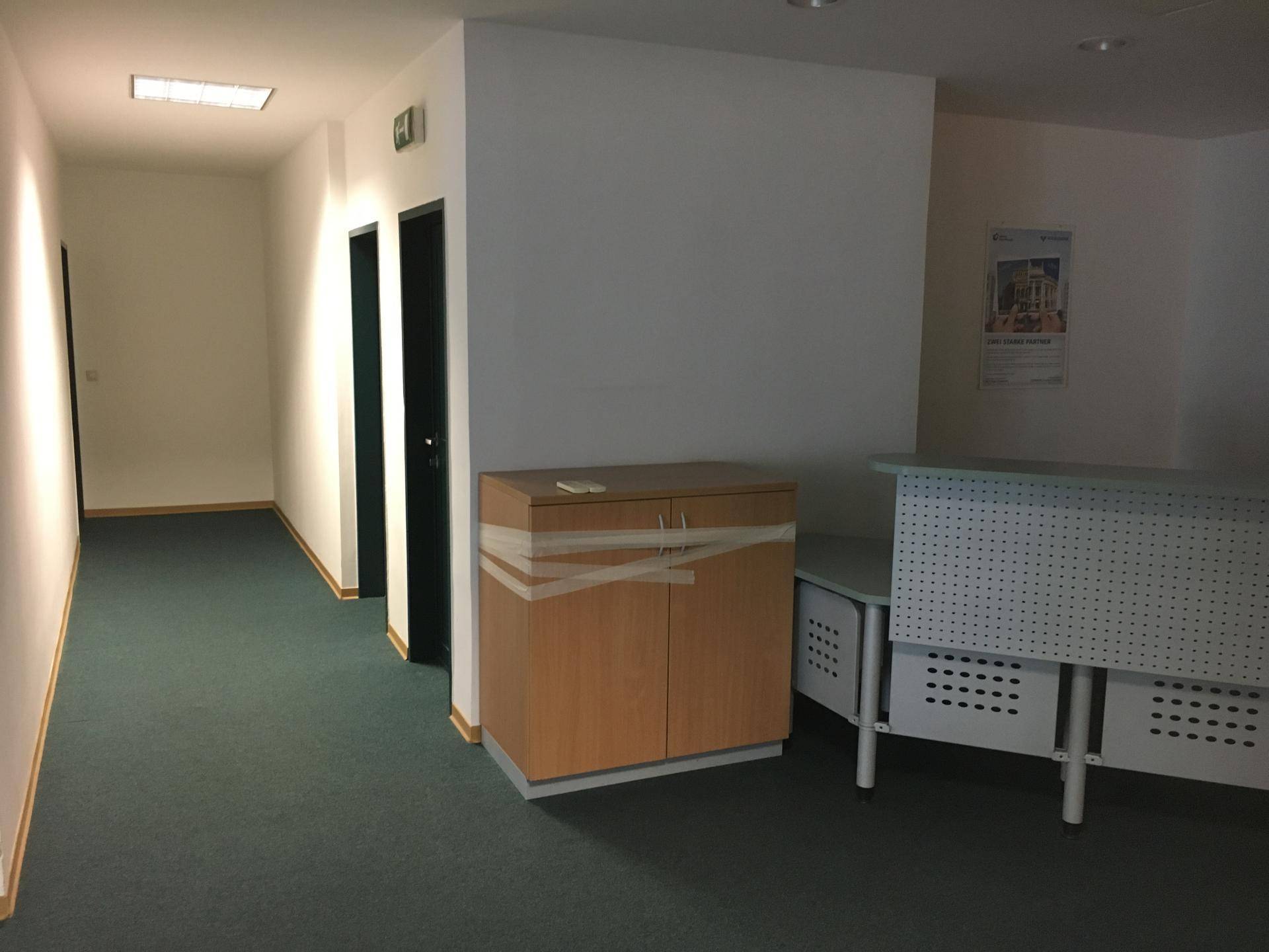 Flur mit dunkelgrünem Teppichboden, weißen Wänden und einem Empfangstresen.