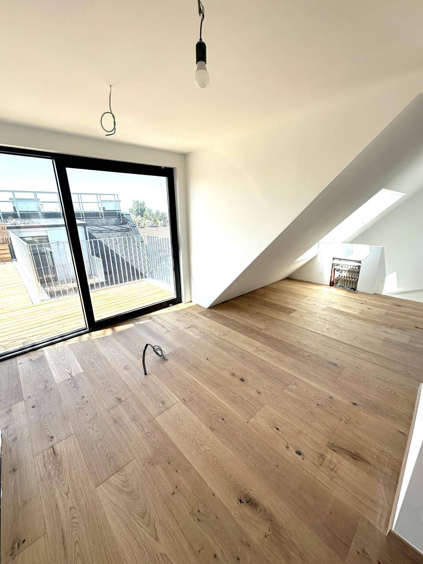 Heller Wohnraum im Dachgeschoss mit Holzboden, großen Schiebetüren zur Terrasse und schrägen Wänden.