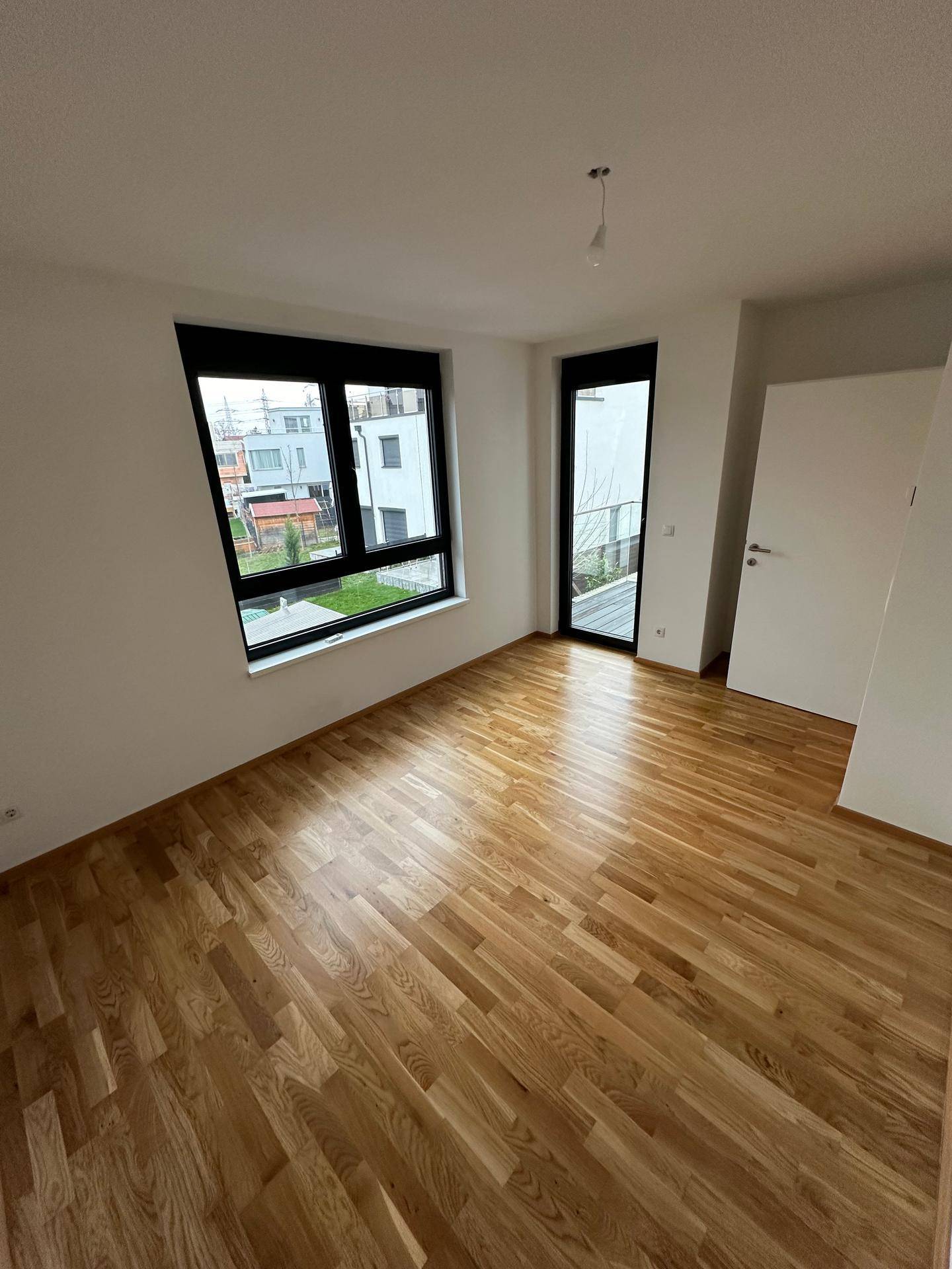 Geräumiges Zimmer mit Holzboden, großem Fenster und Zugang zu einem französischen Balkon.
