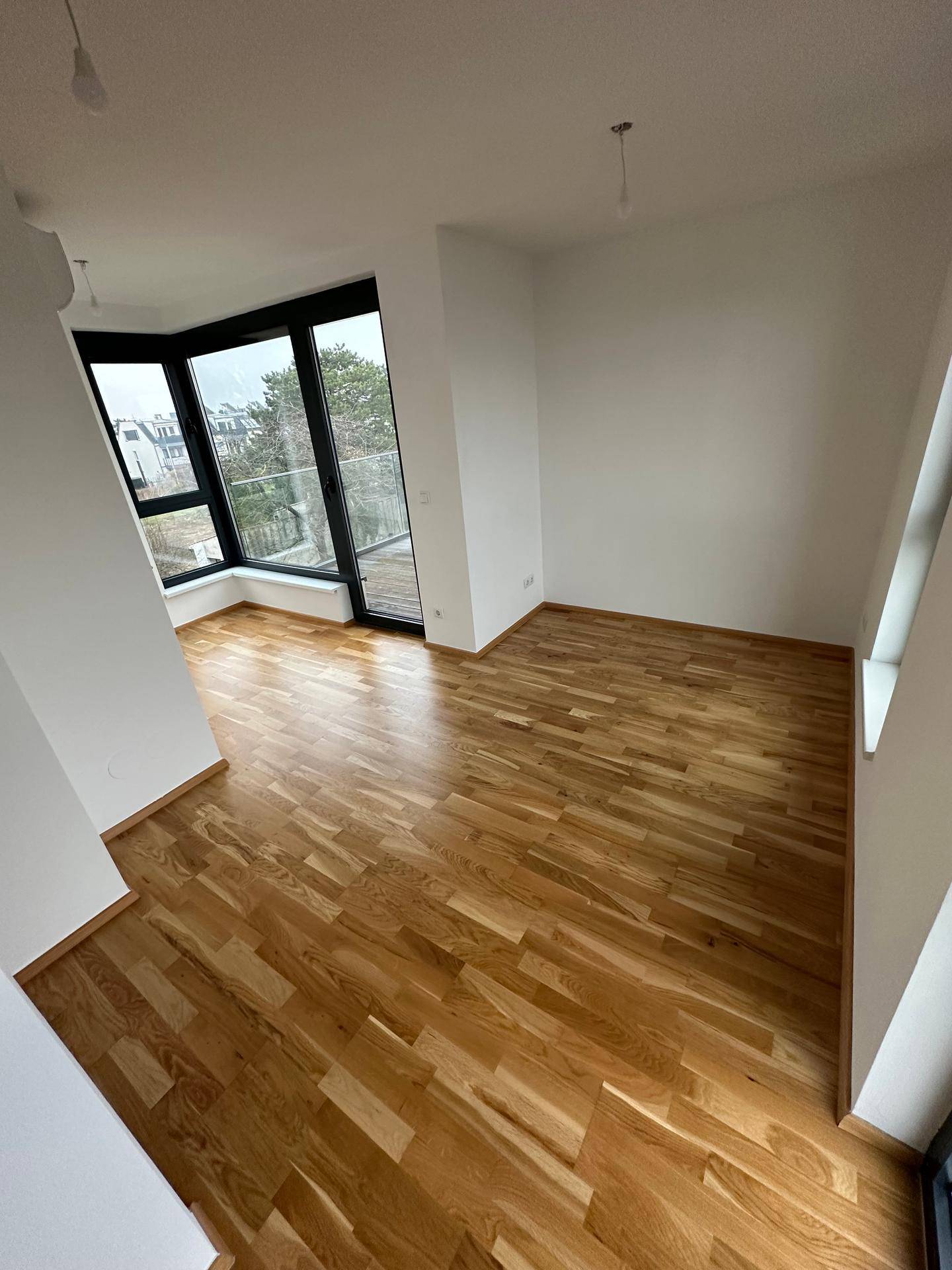 Helles Zimmer mit Holzboden und großen Fenstern, inklusive Zugang zu einem französischen Balkon.