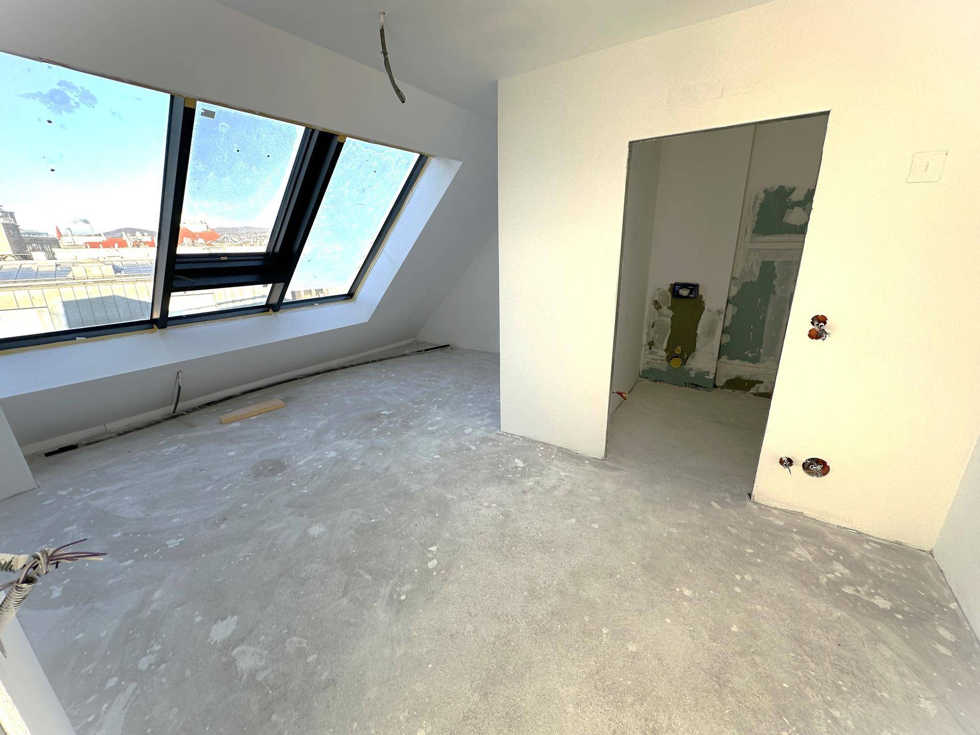 Rohbauzimmer mit großem Dachfenster, das viel Licht spendet, und vorbereiteten Wänden für den Innenausbau.