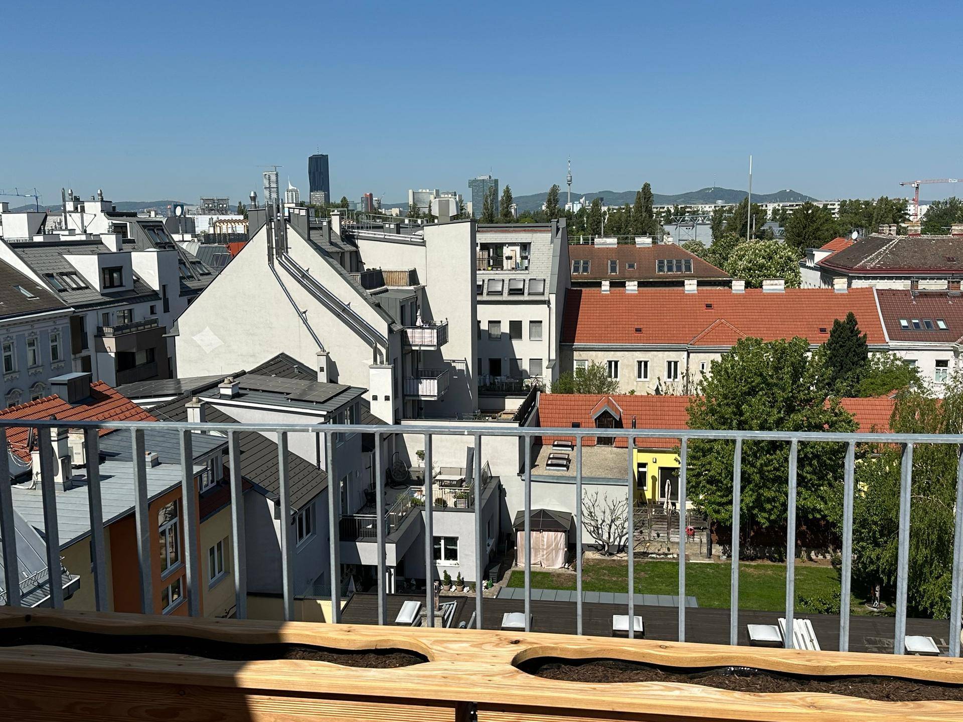 Weitläufiger Blick von einem Balkon über die Dächer der Stadt und grüne Innenhöfe.