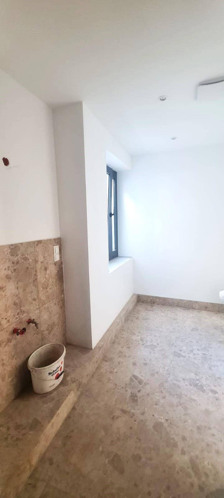 Helles Badezimmer im Rohbau mit Fliesenboden und einem Fenster für natürliche Belüftung.