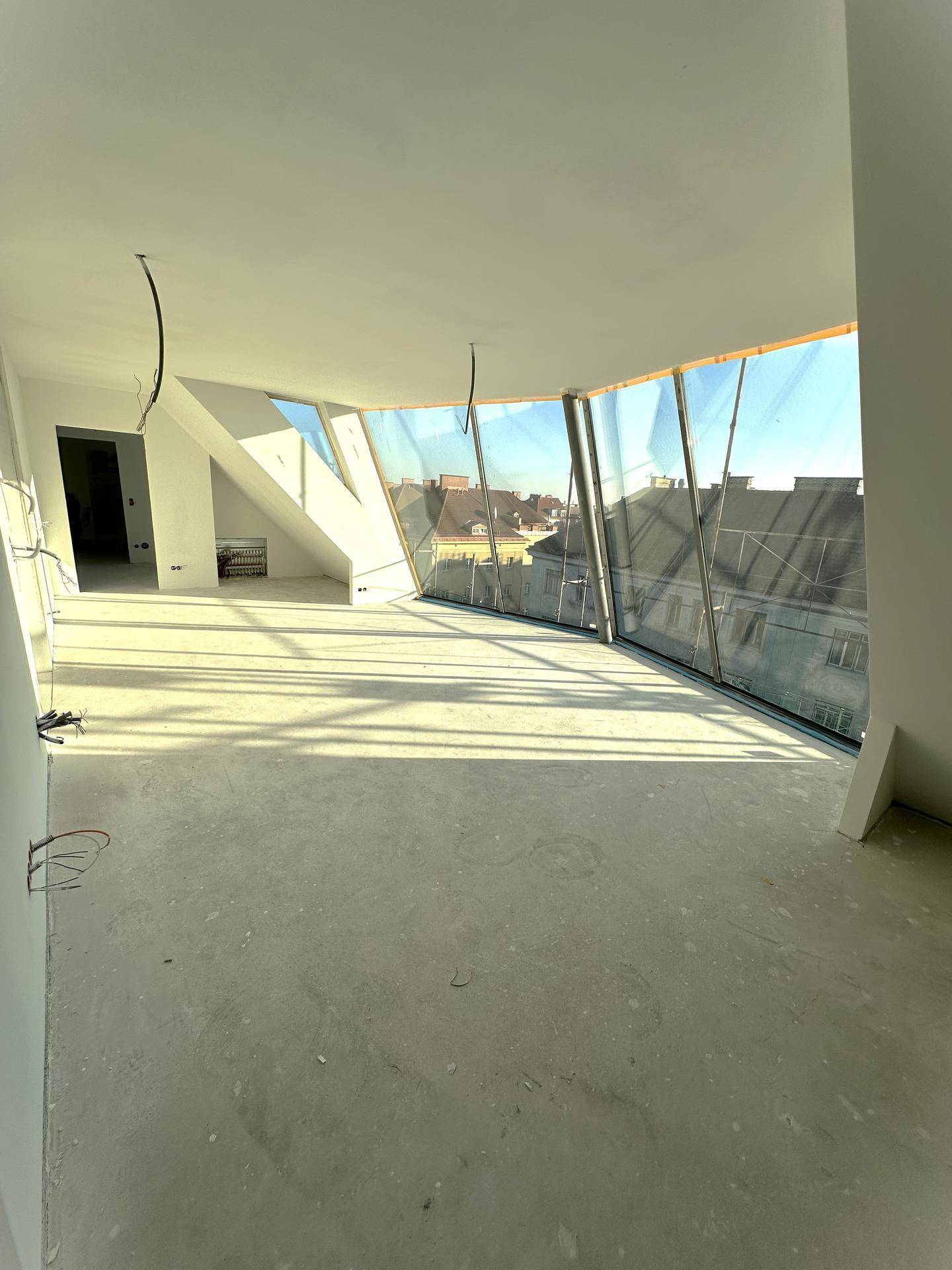 Geräumiger Rohbau mit einzigartigen, geschwungenen Fensterfronten, die viel Tageslicht hereinlassen und Stadtblick bieten.
