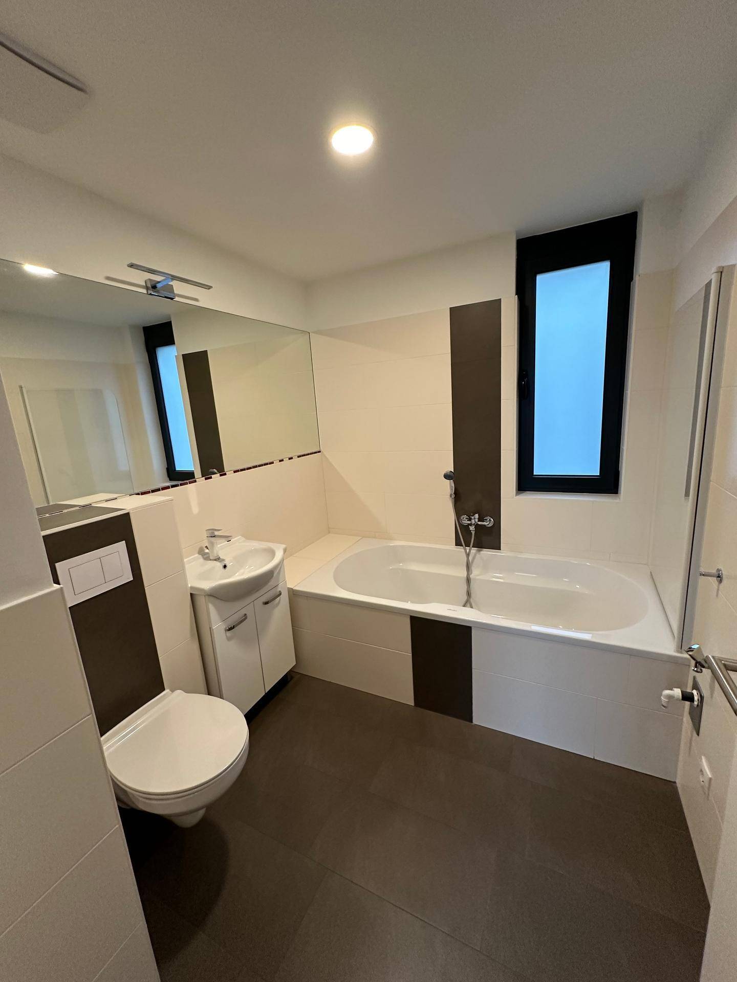 Modernes Badezimmer mit Badewanne, WC, Einzelwaschbecken und Fenster in neutralen Farben.