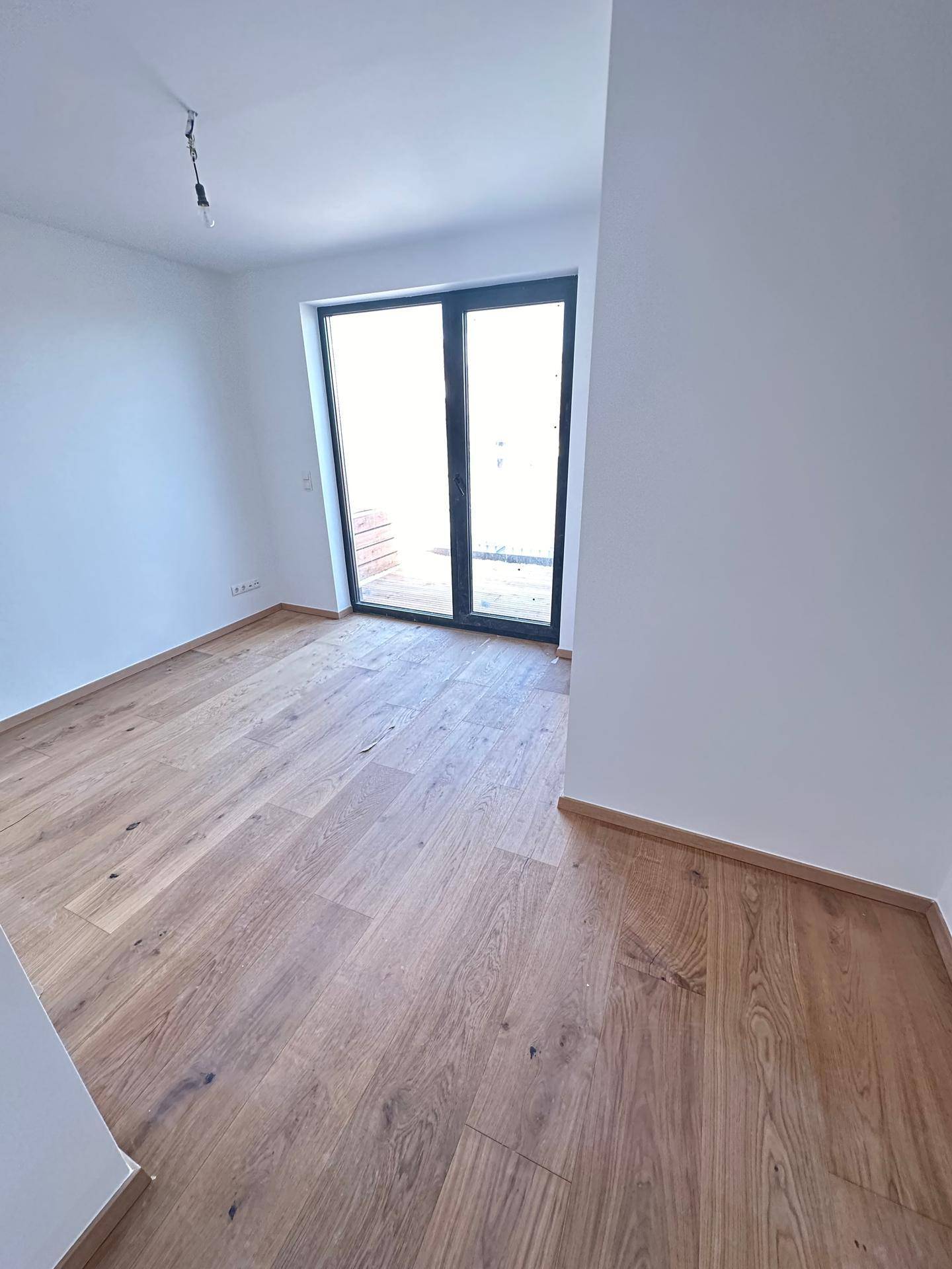 Geräumiges Schlafzimmer mit Holzboden und großer Schiebetür, die Zugang zu einem Außenbereich bietet.