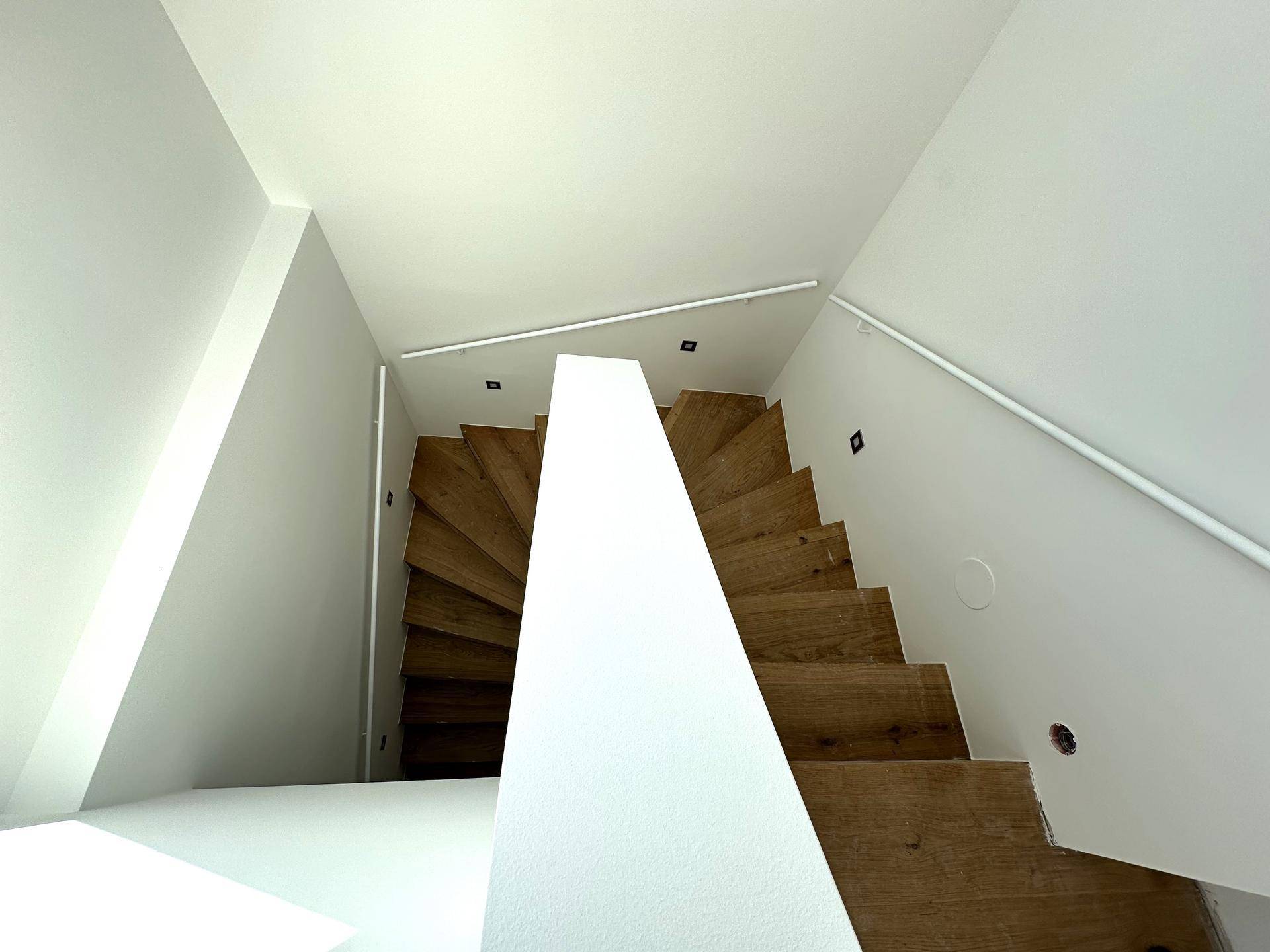 Moderne Holztreppe mit weißem Geländer und indirekter Beleuchtung, die in die obere Etage führt.