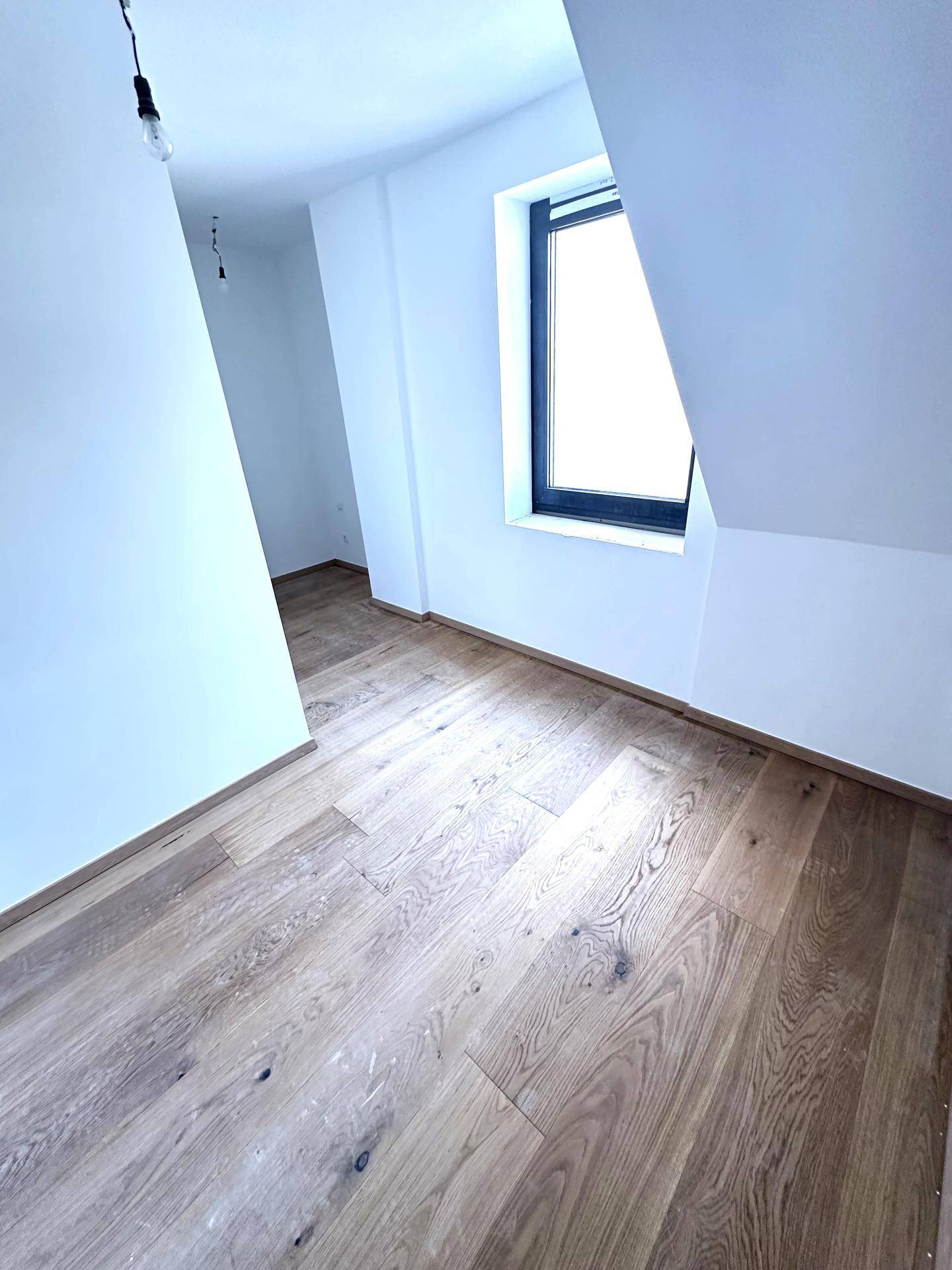 Helles Schlafzimmer im Dachgeschoss mit Holzboden, einem Fenster und schrägen Wänden.