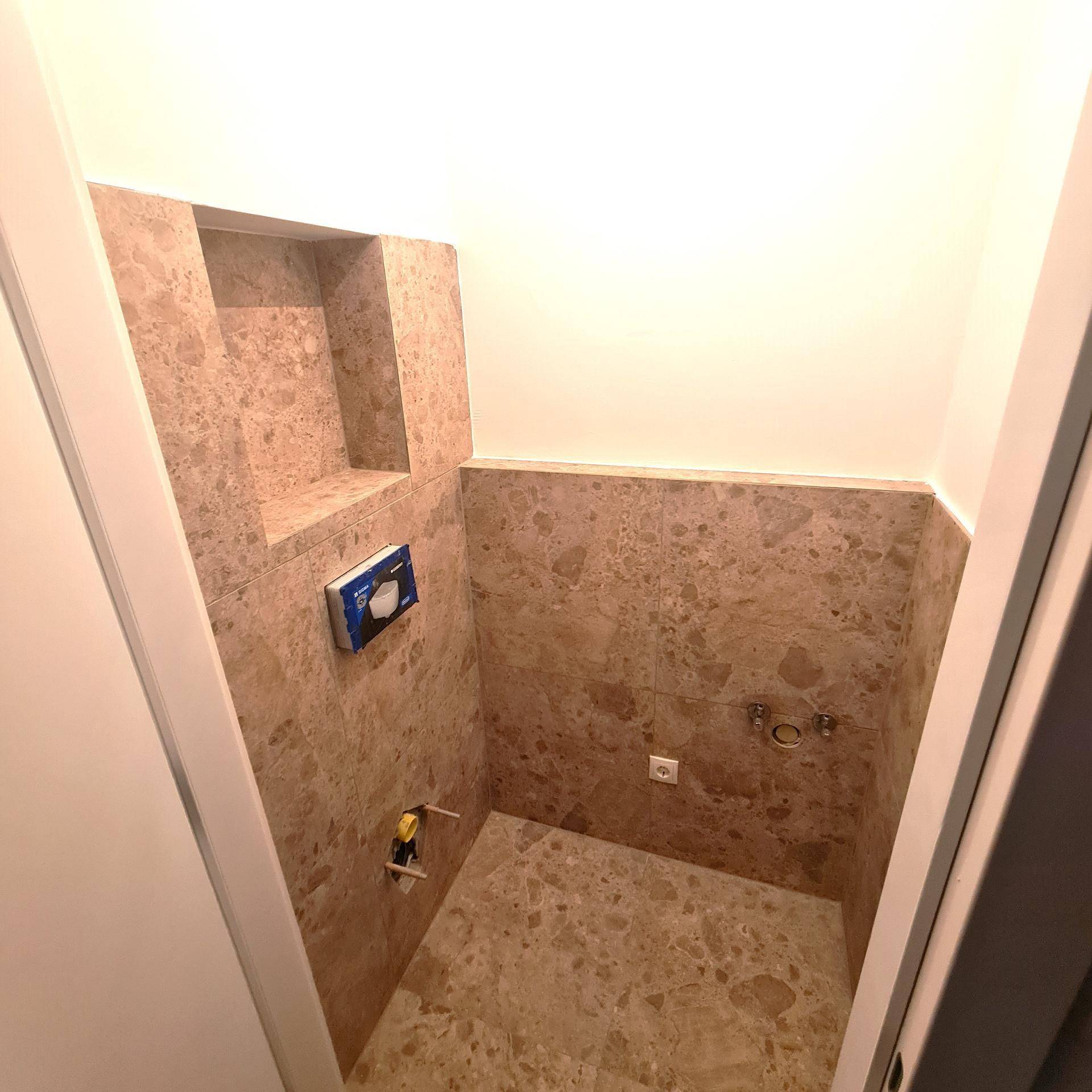 Gäste-WC im Rohbau mit modernen Fliesen und Vorbereitung für ein Wand-WC.