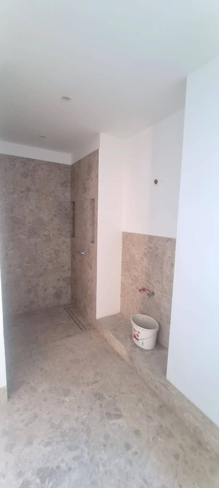 Unfertiges Badezimmer mit modernen Fliesen und vorbereitetem Bereich für eine begehbare Dusche.
