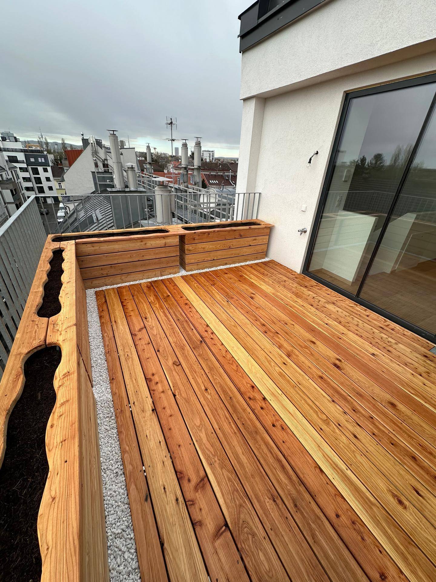 Geräumige Terrasse mit Holzbelag und integrierten Pflanzkästen, umgeben von Dächern.