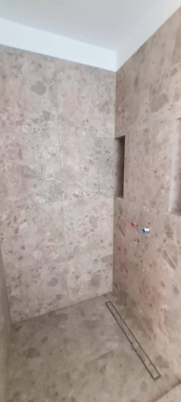 Detailansicht des Duschbereichs im Badezimmer mit großformatigen Fliesen und Bodeneinlauf.