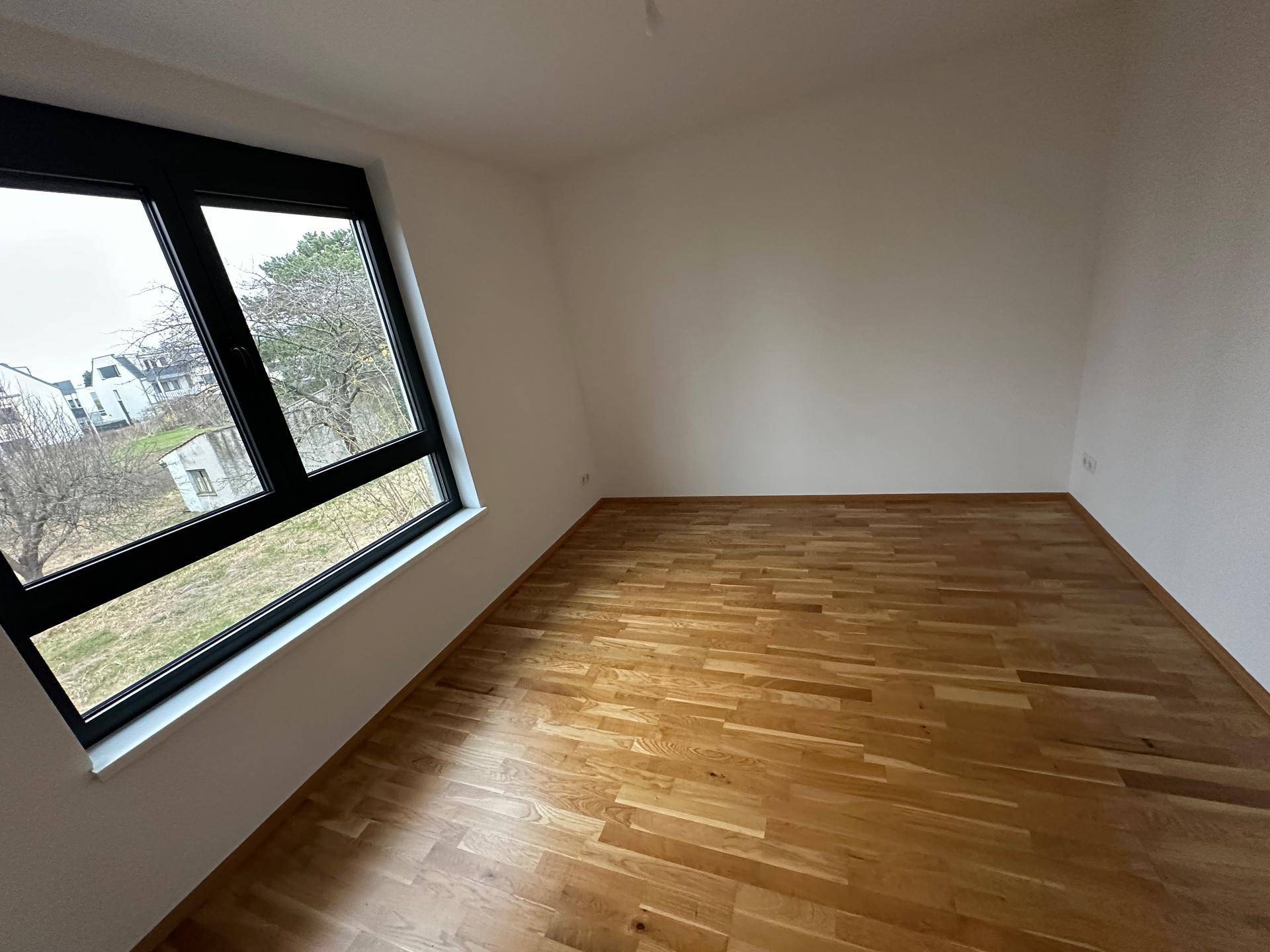 Helles Zimmer mit Eichenparkett und großem Fenster mit Blick ins Grüne.