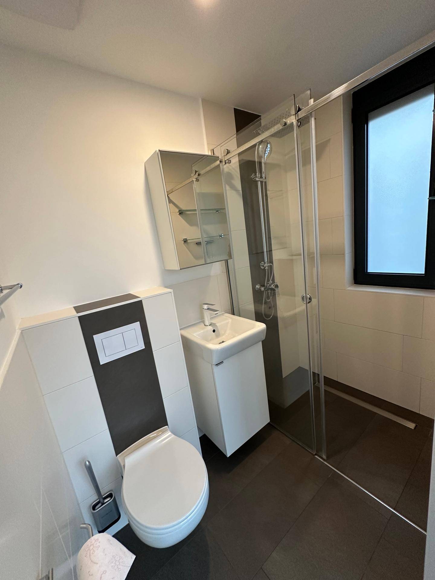Modernes Badezimmer mit ebenerdiger Dusche, WC, Einzelwaschbecken und Fenster.