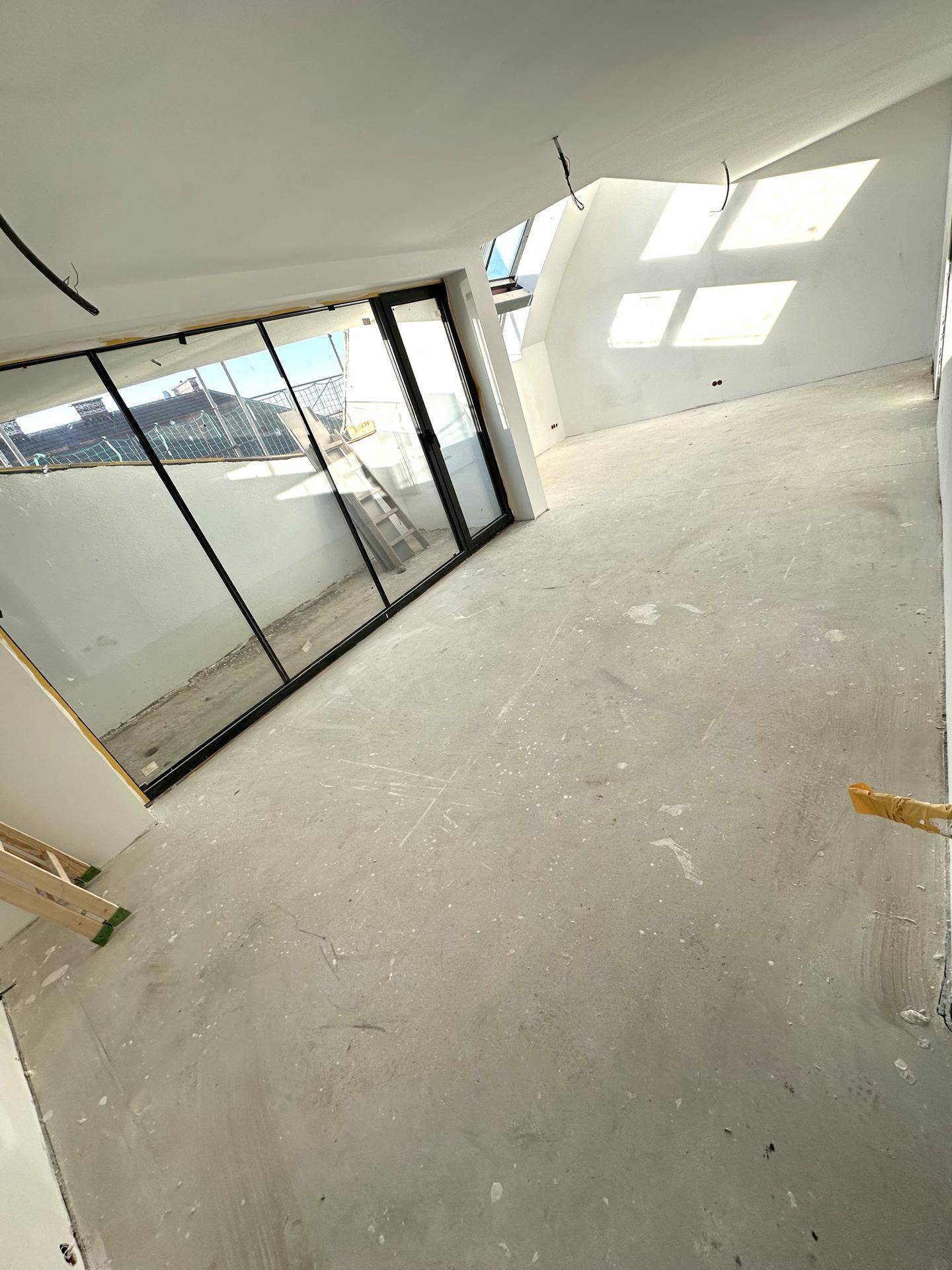 Unfertiger Raum mit Zugang zu einem Außenbereich und viel Tageslicht durch große Fenster und Dachfenster.
