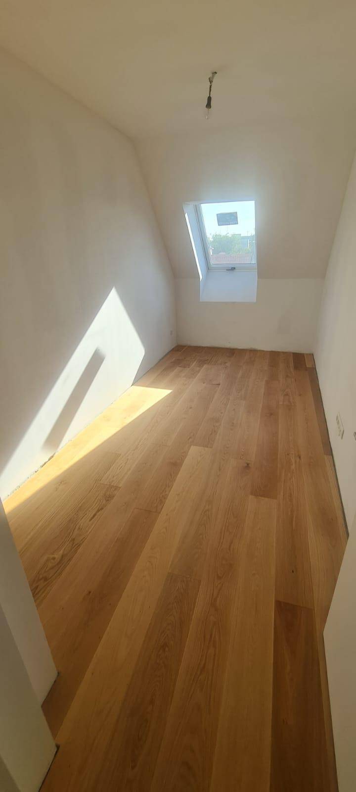 Sonniger Raum im Dachgeschoss mit Holzparkett und viel Tageslicht durch das Dachfenster.