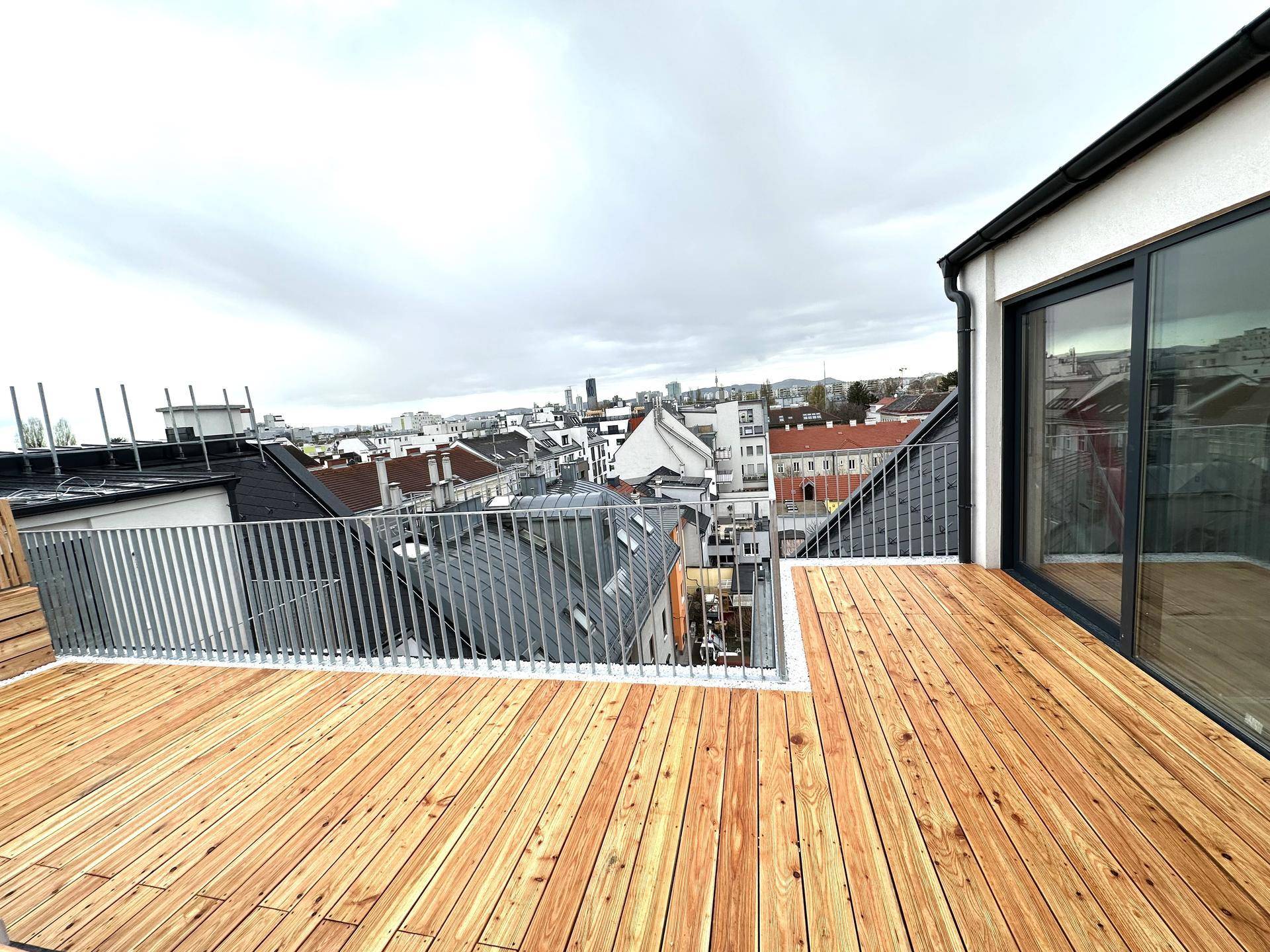 Geräumige Dachterrasse mit Holzboden und Metallgeländer, bietet einen weiten Blick über die Stadt.