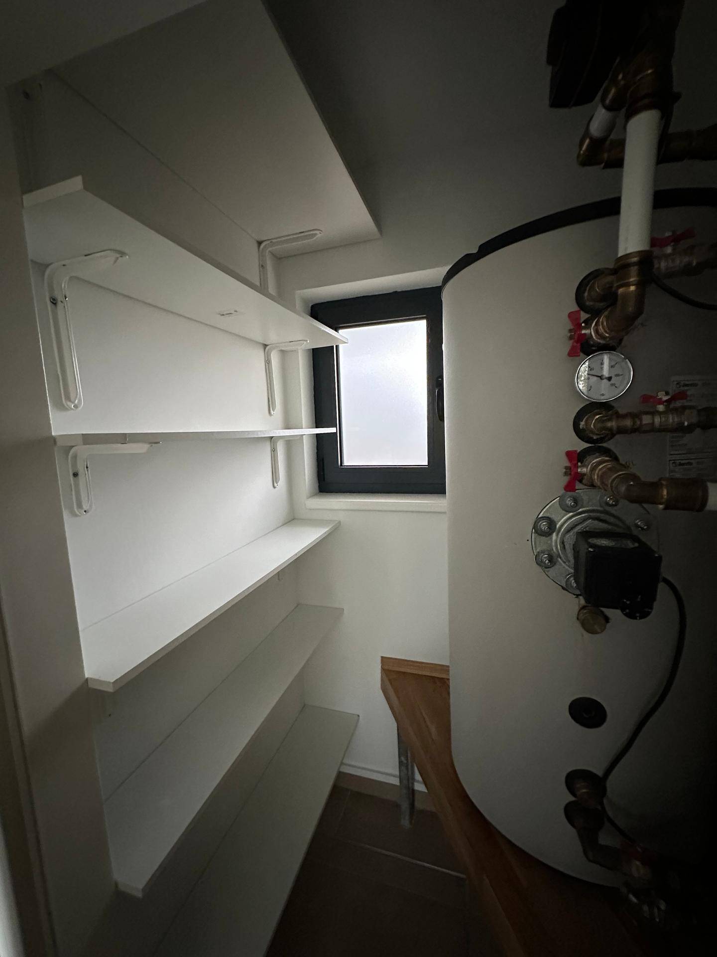 Praktischer Hauswirtschaftsraum mit Warmwasserspeicher, Regalen und kleinem Fenster.