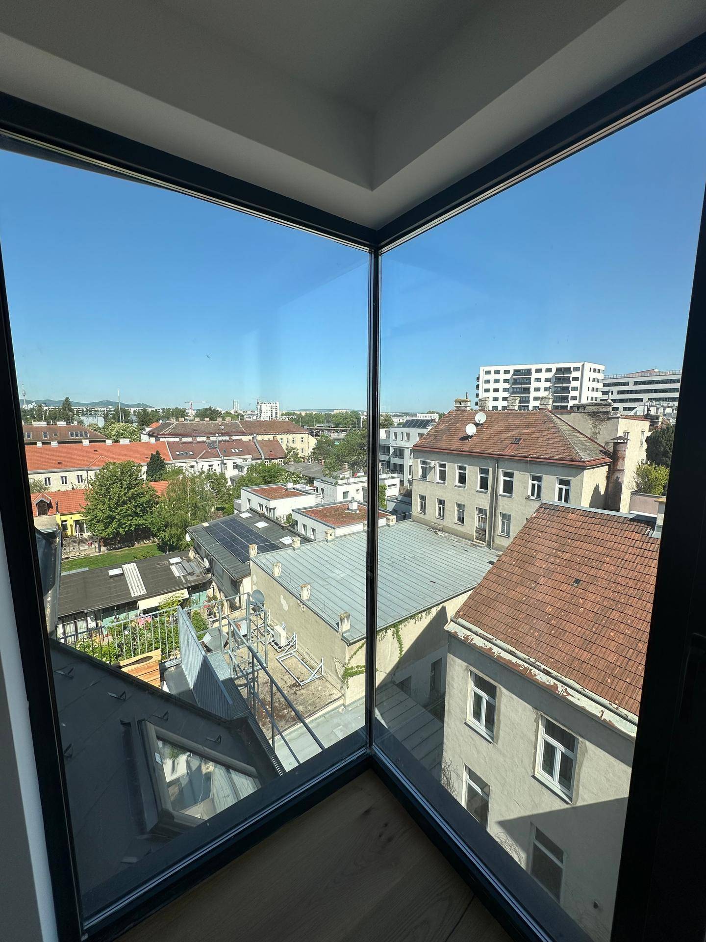 Eckfenster mit weitem Blick über die Dächer der Stadt und umliegende Gebäude an einem sonnigen Tag.