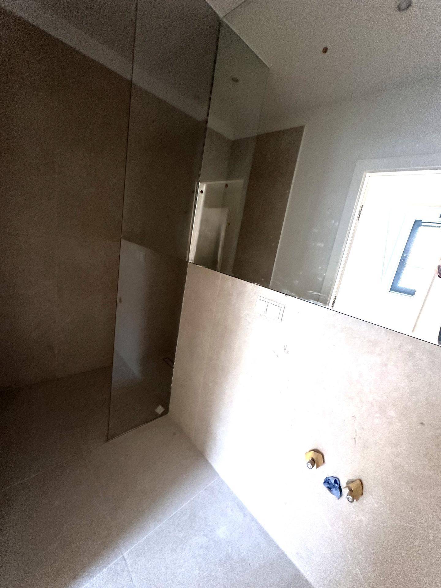 Modernes Badezimmer mit beigefarbenen Fliesen, großem Spiegel und vorbereitetem Duschbereich.