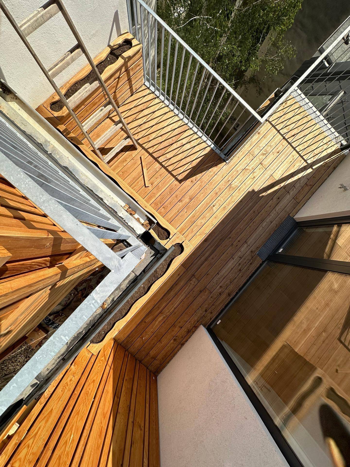 Blick von oben auf eine Holzterrasse mit modernen Metallgeländern und Treppenzugang.