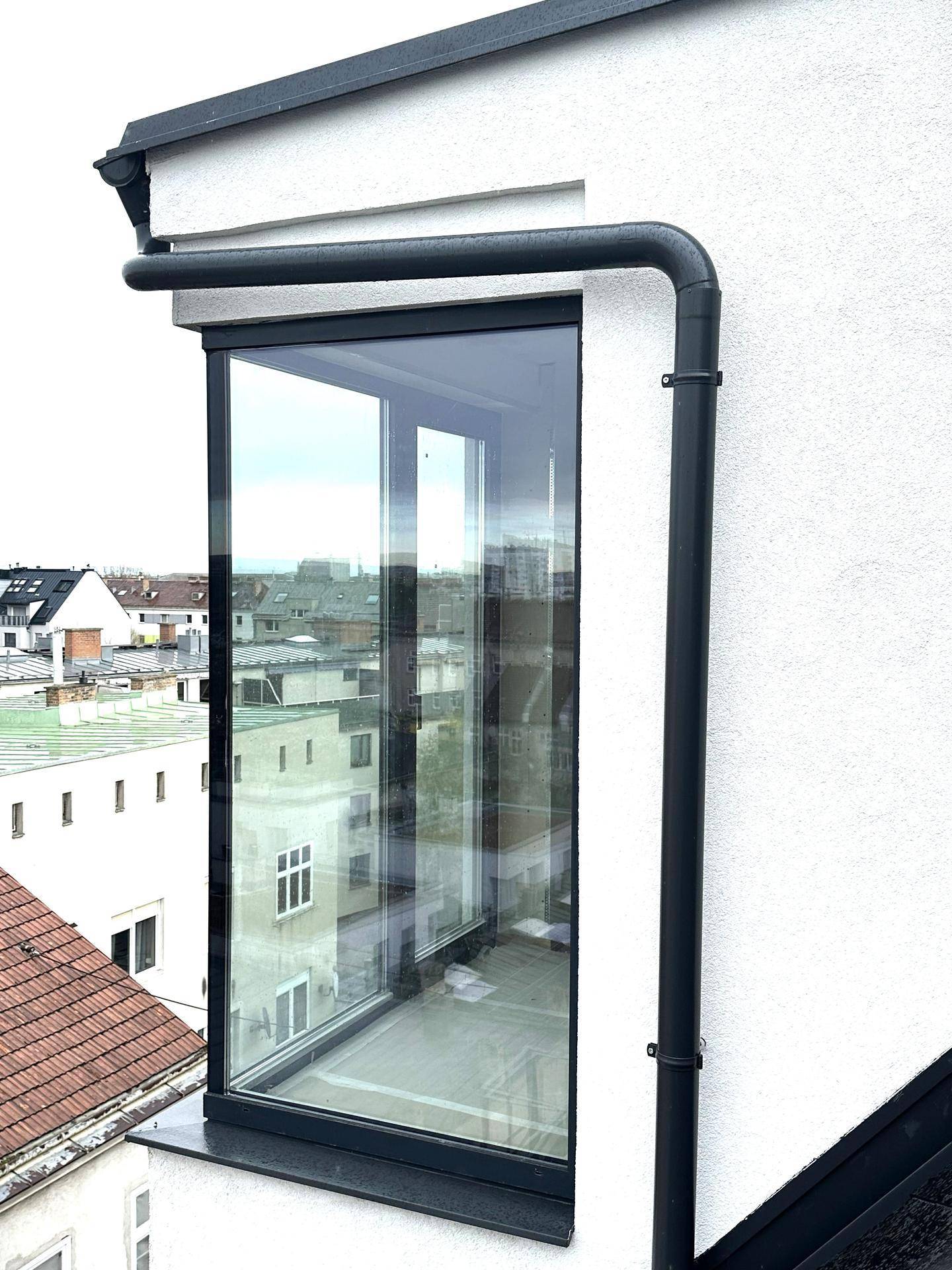 Moderne Fensterfront an der Gebäudefassade mit schwarzem Rahmen und Blick auf die Stadt.