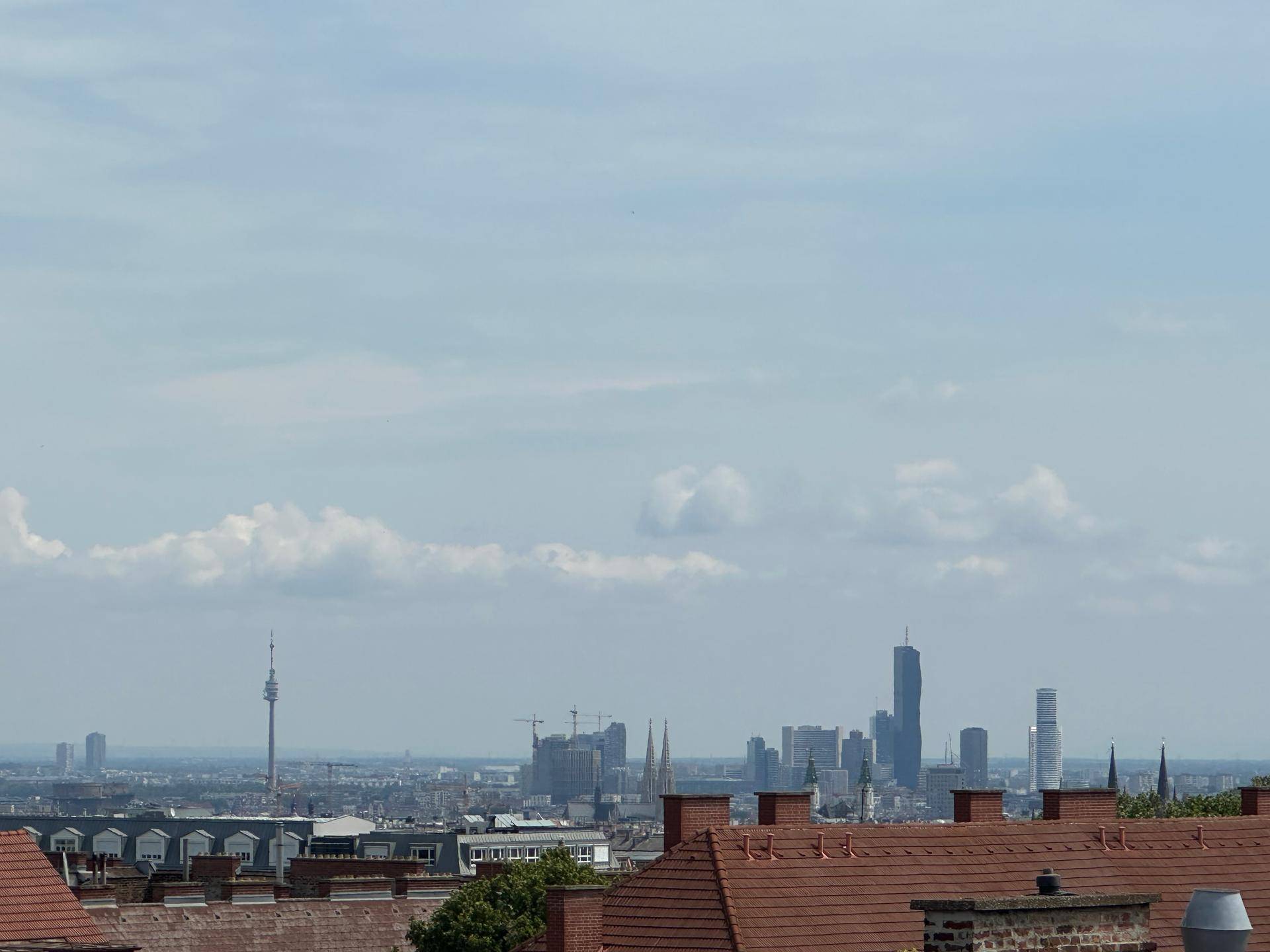 Weitblick über die Stadt mit moderner Skyline, Hochhäusern und einem Fernsehturm unter bewölktem Himmel.