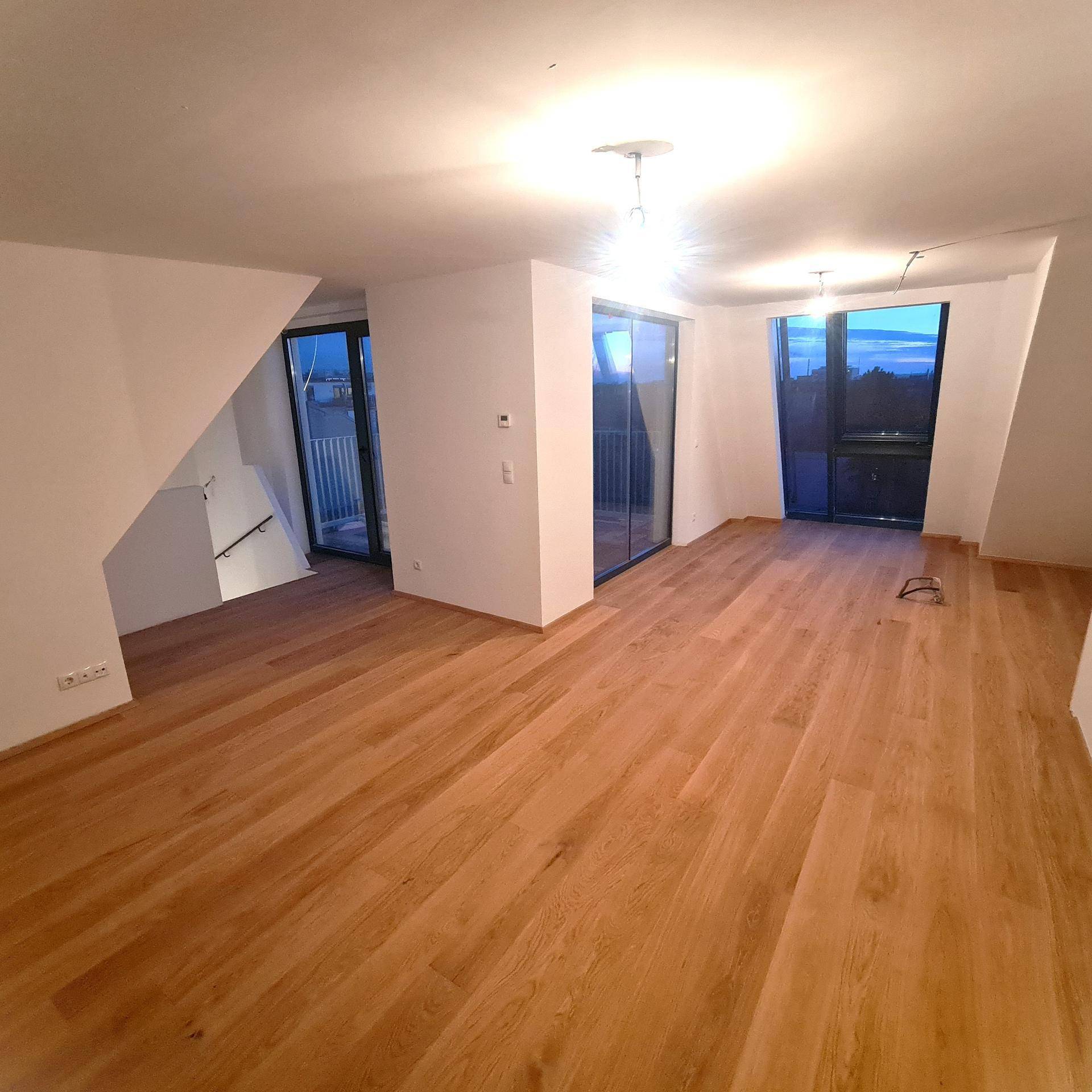 Heller Wohnraum mit neuem Holzparkettboden und Zugang zu einem Außenbereich.